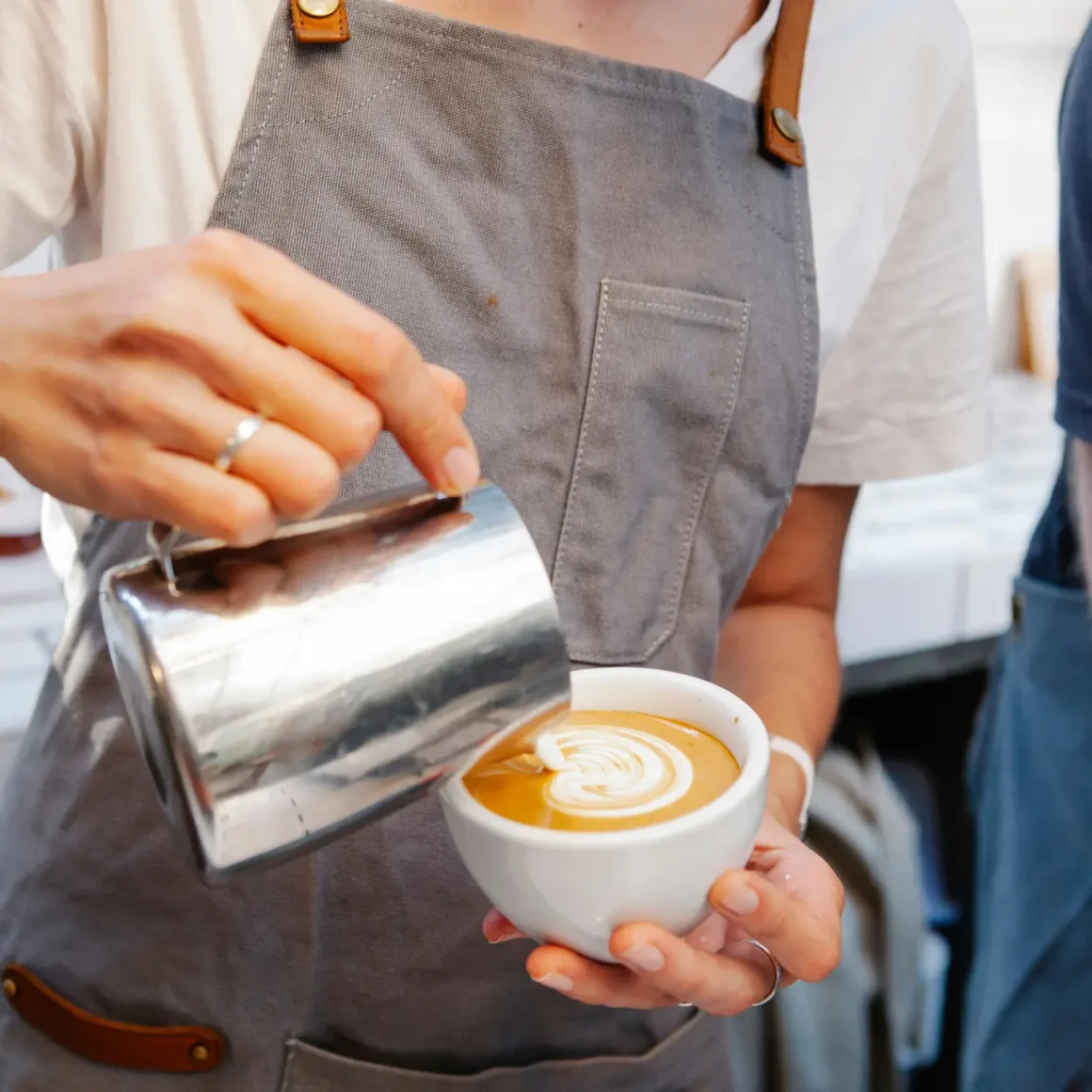 barista pouring milk into a cup of coffee