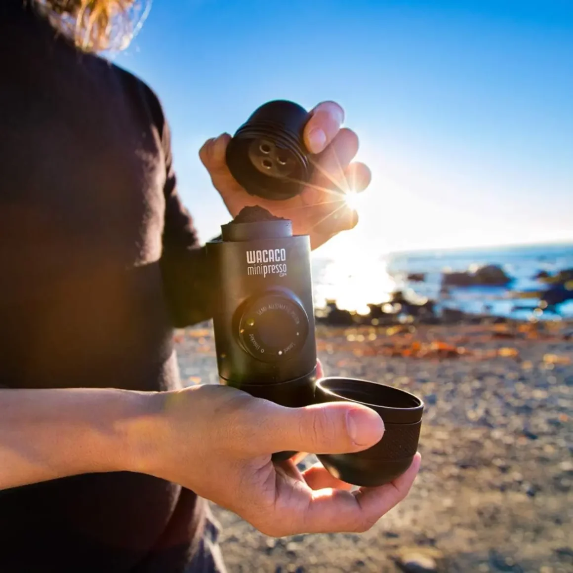 a person holding a small coffee maker on a beach