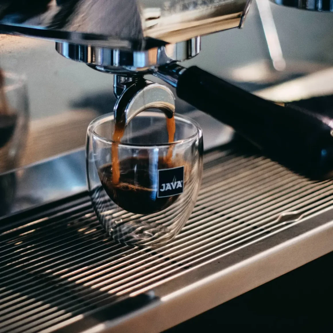 an espresso machine pouring a glass of dark roast coffee