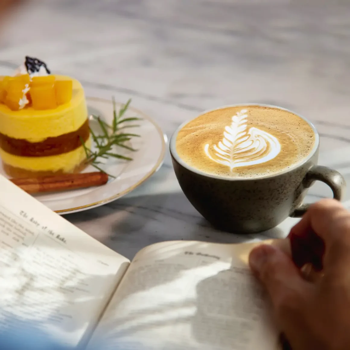 a person reading a book and a cup of cappuccino coffee