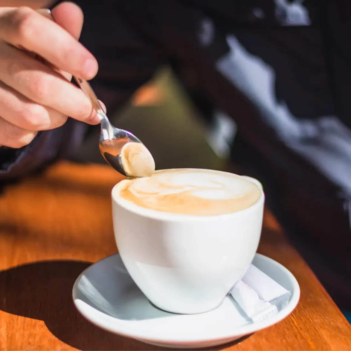 a person pouring a spoon into a cup of café con leche coffee