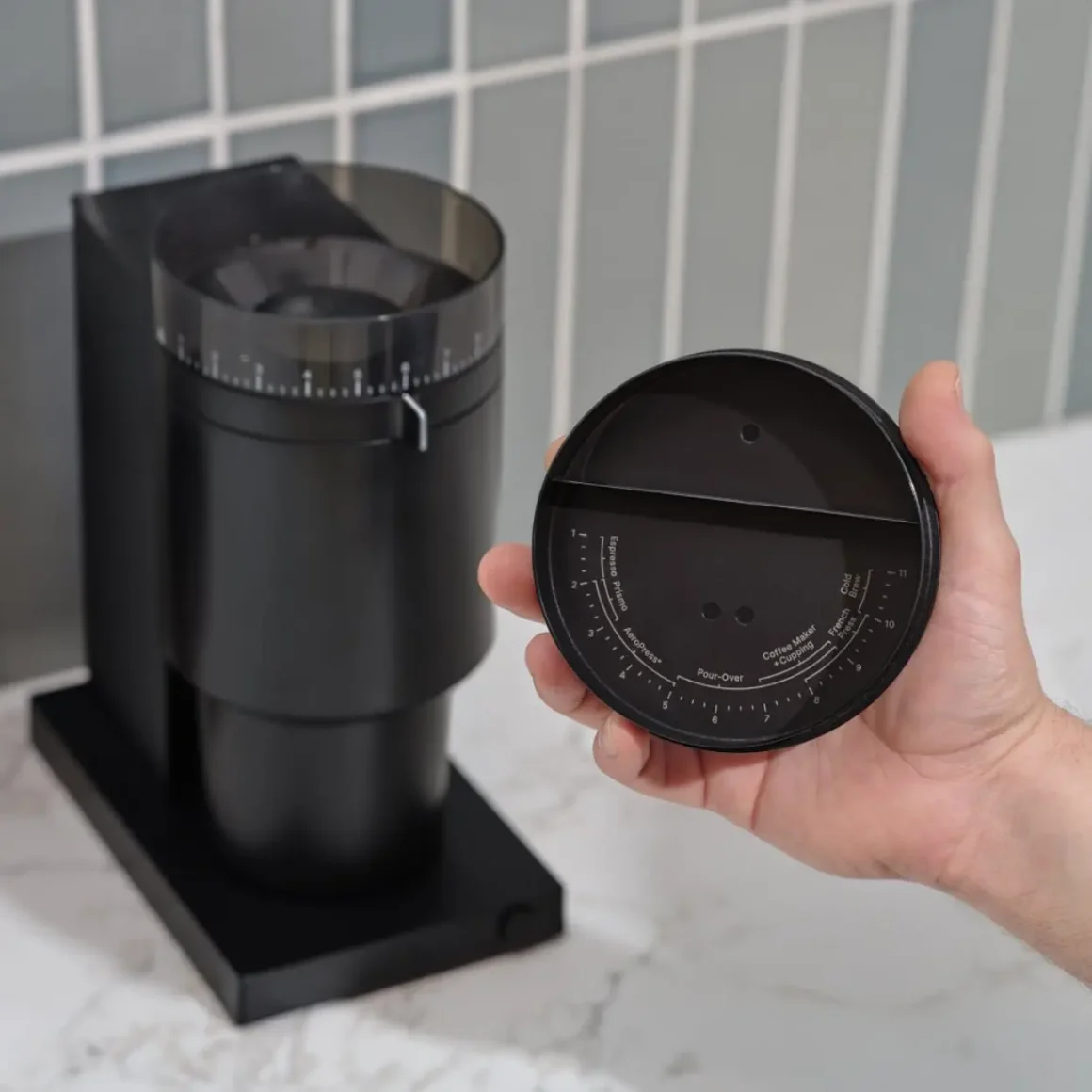 a hand holding a cap of a coffee burr grinder placed on a counter