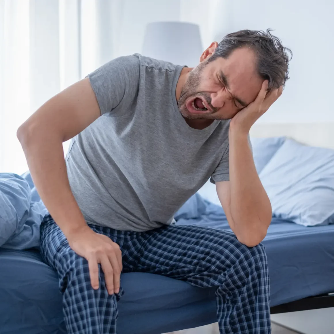 a man sitting on a bed yawning