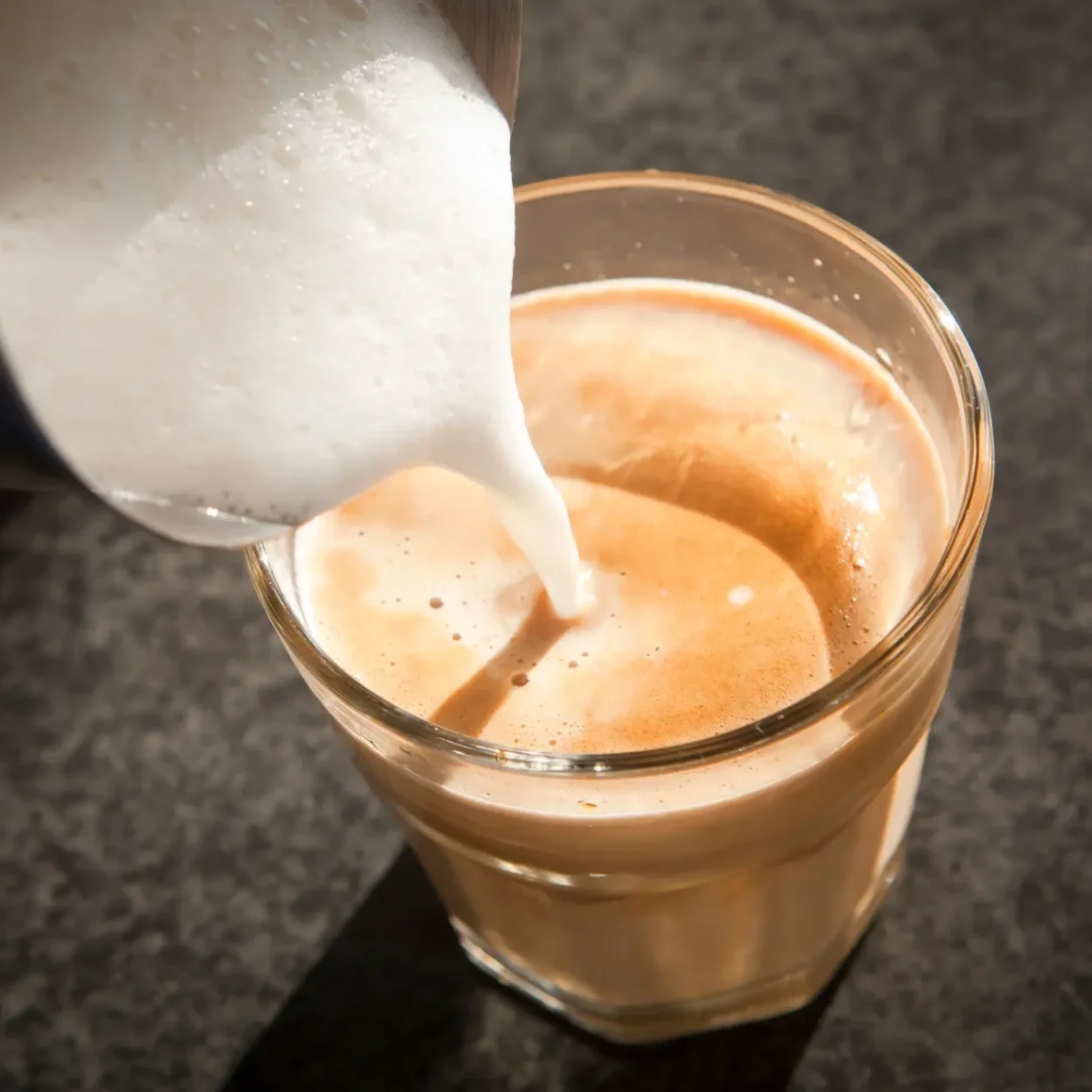 a pouring milk into a glass of latte