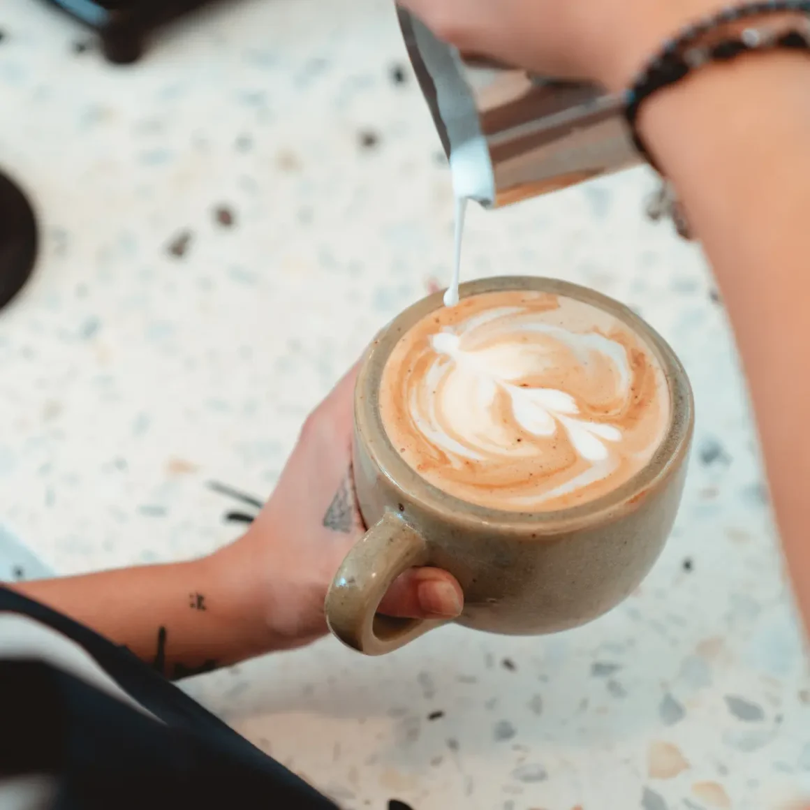 barista pouring milk into a cup of cappuccino coffee