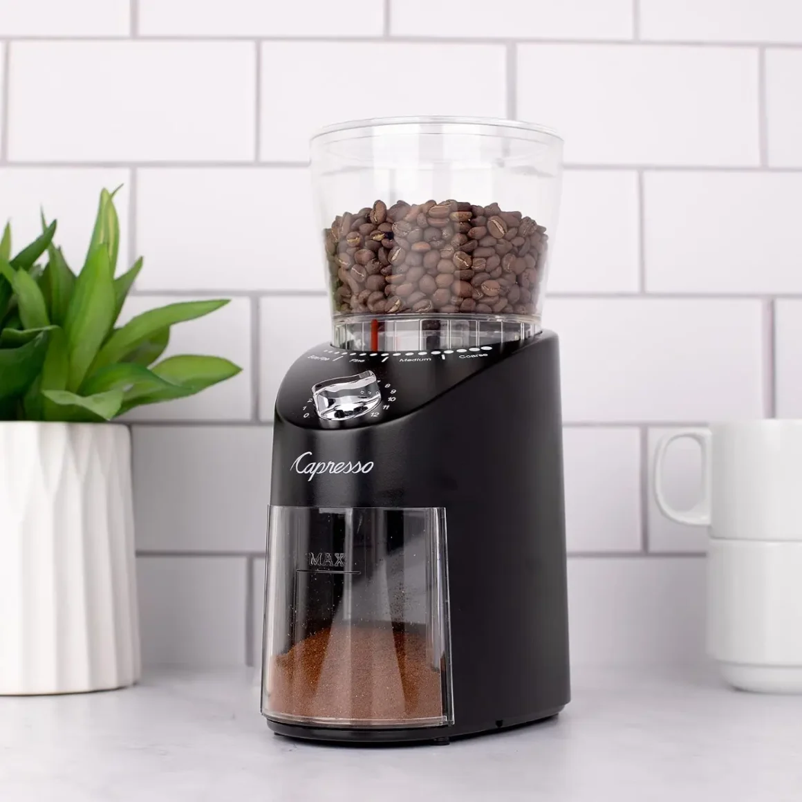 a capresso infinity plus black conical burr grinder with coffee beans in it