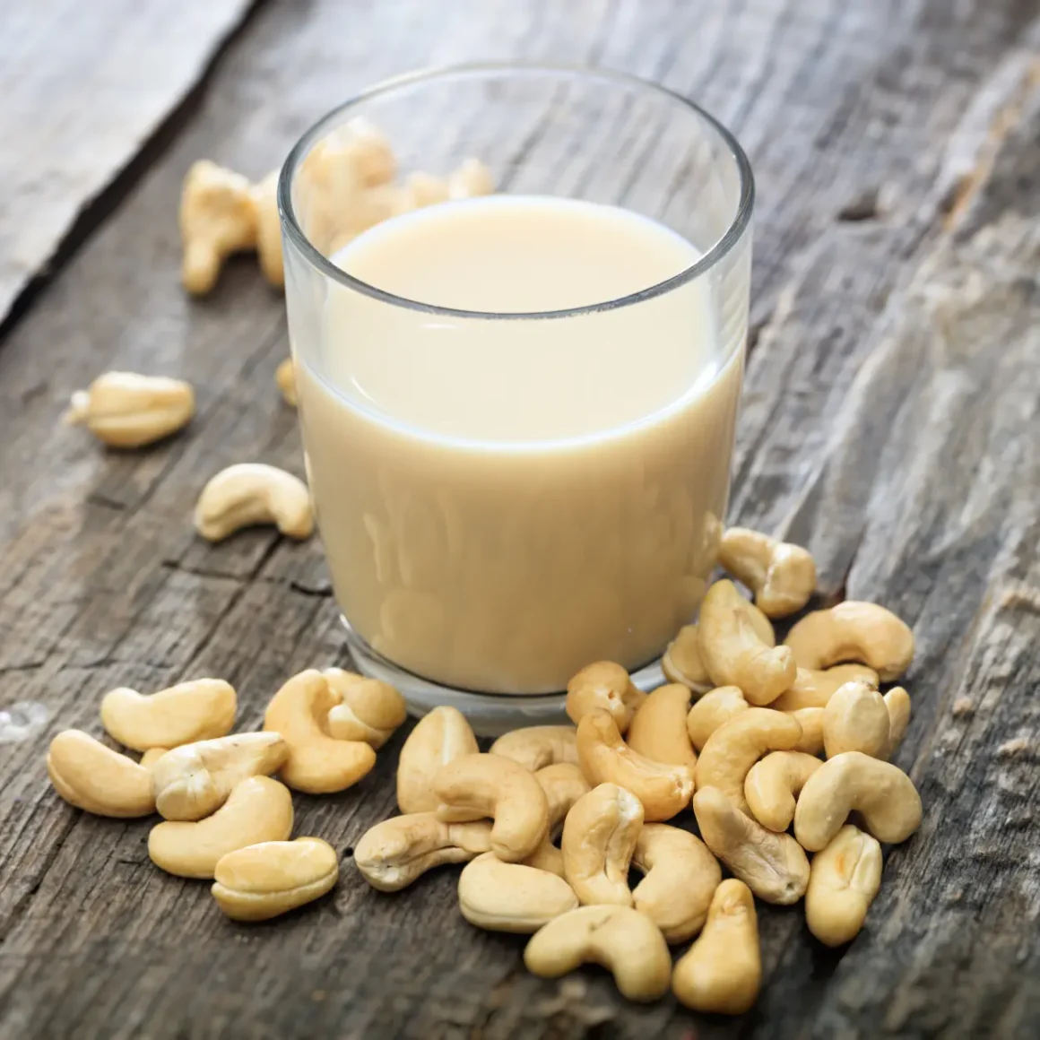 a glass of cashew milk and some cashews on a surface
