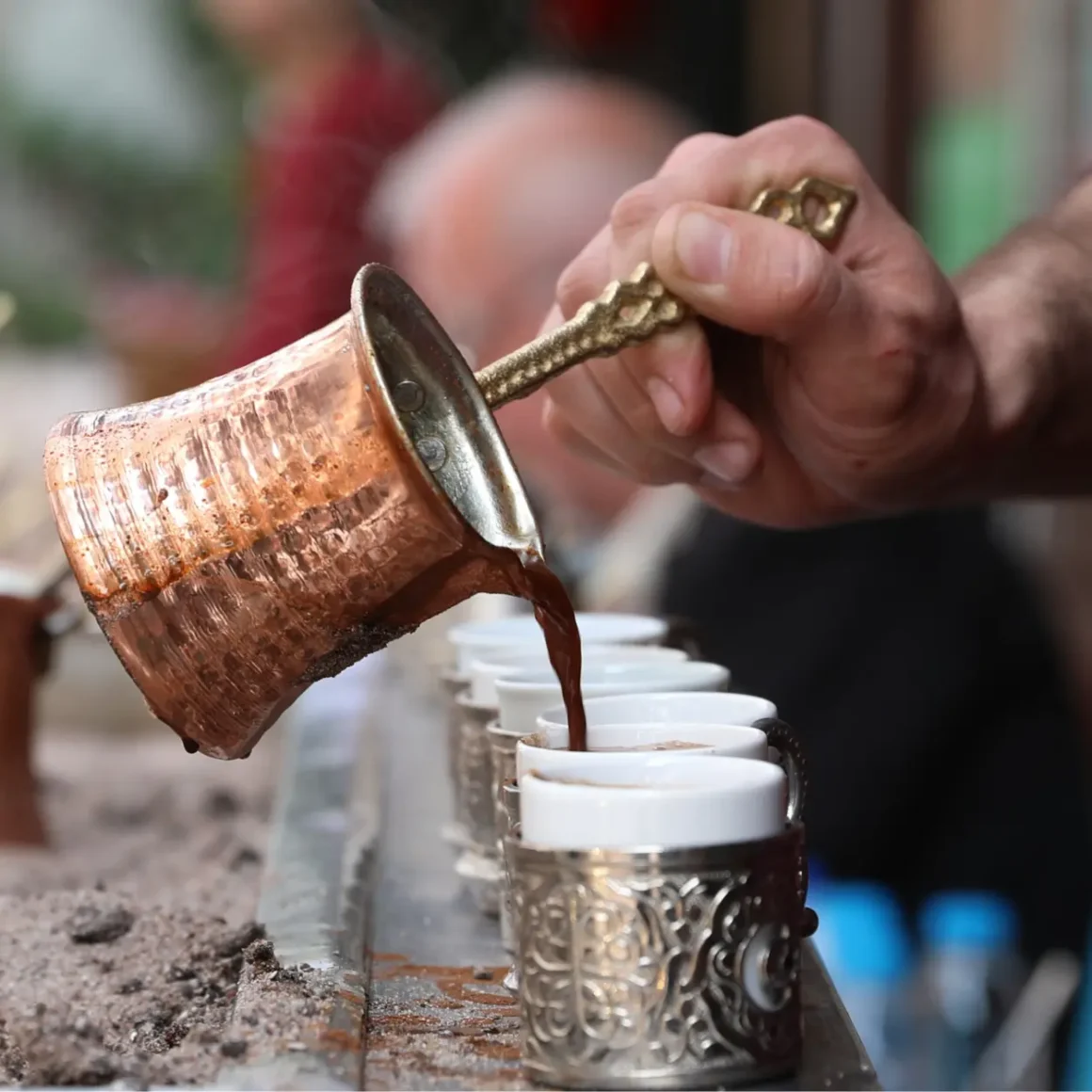 barista pouring coffee from a copper pot into cups