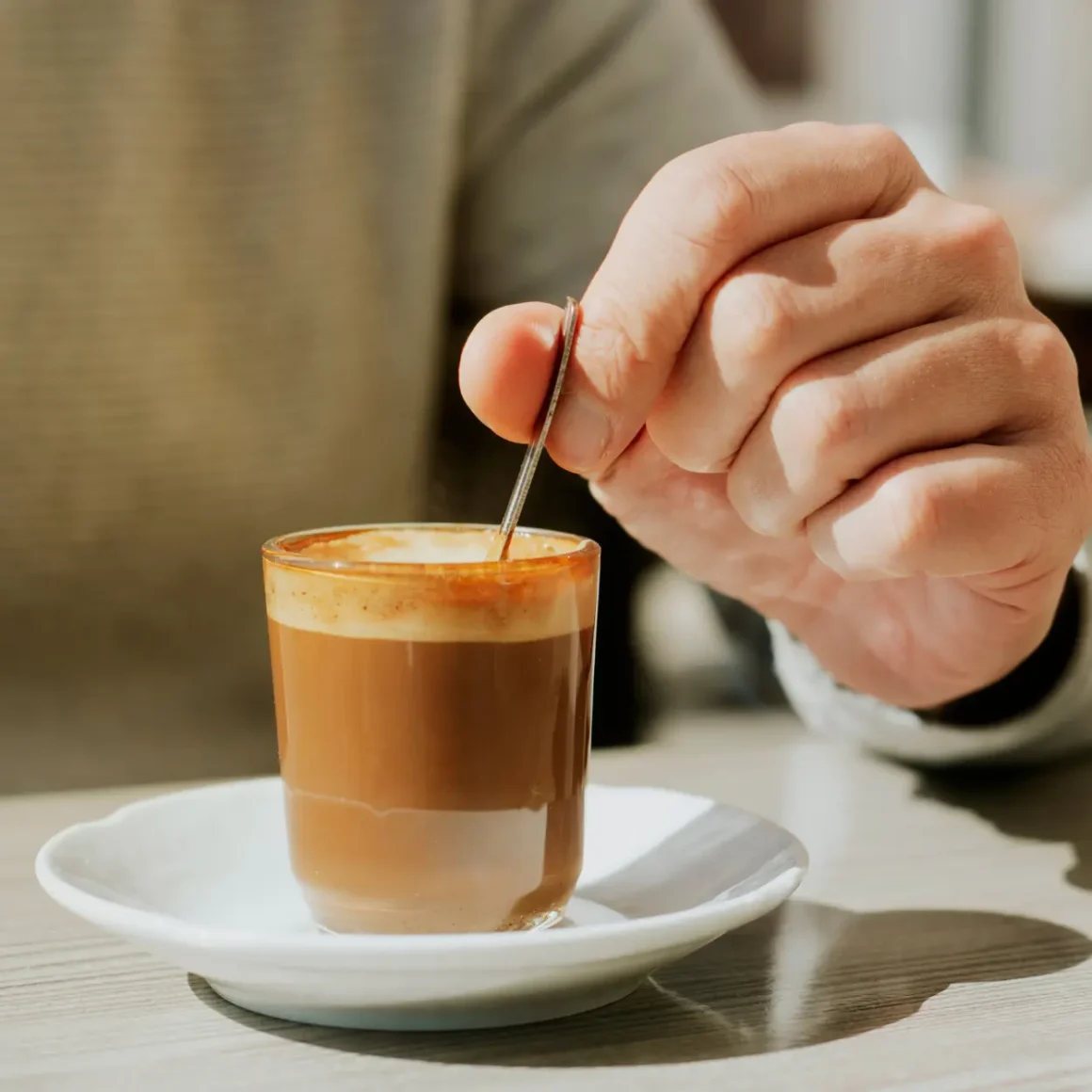 a person holding a spoon in a glass of cortado coffee