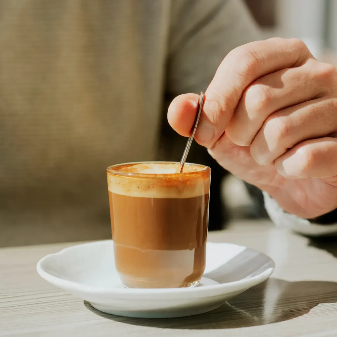 a person holding a spoon in a glass of cortado coffee