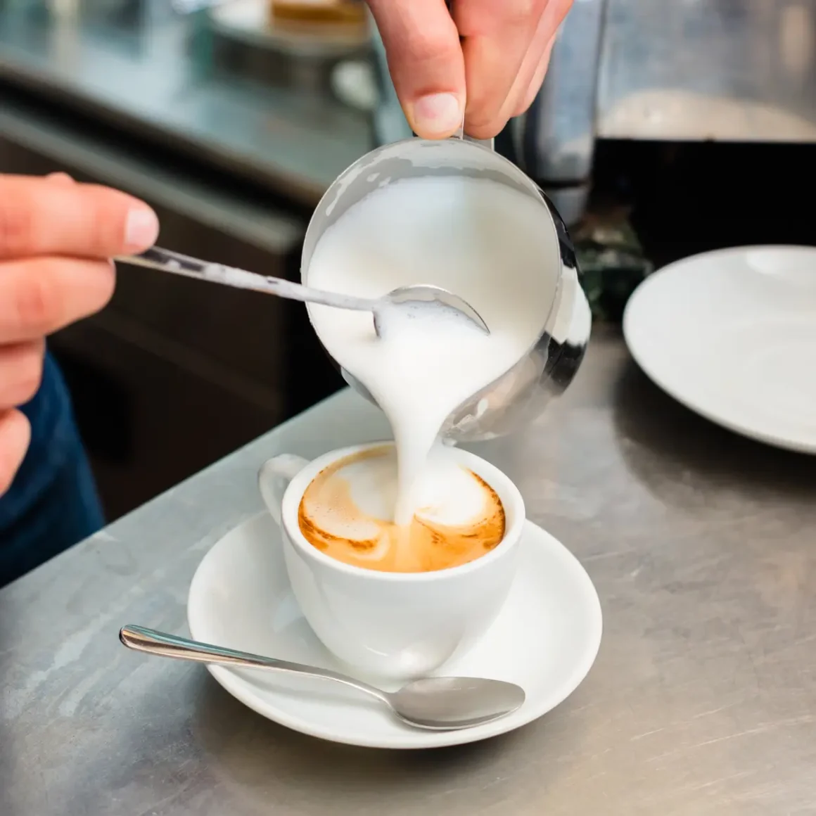 barista brewing dry cappuccino by pouring milk into a cup of coffee