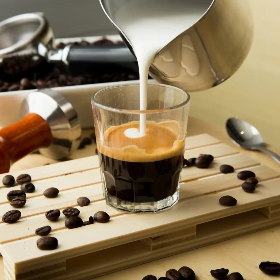 milk is being poured into a glass of cortado coffee