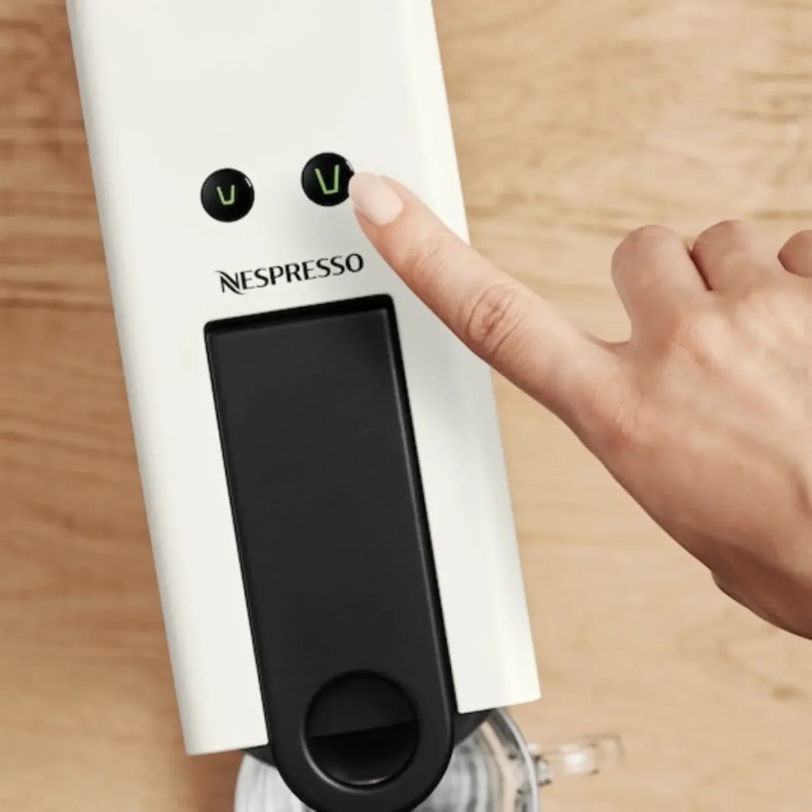 a person's finger pointing at a nespresso essenza mini espresso machine by breville