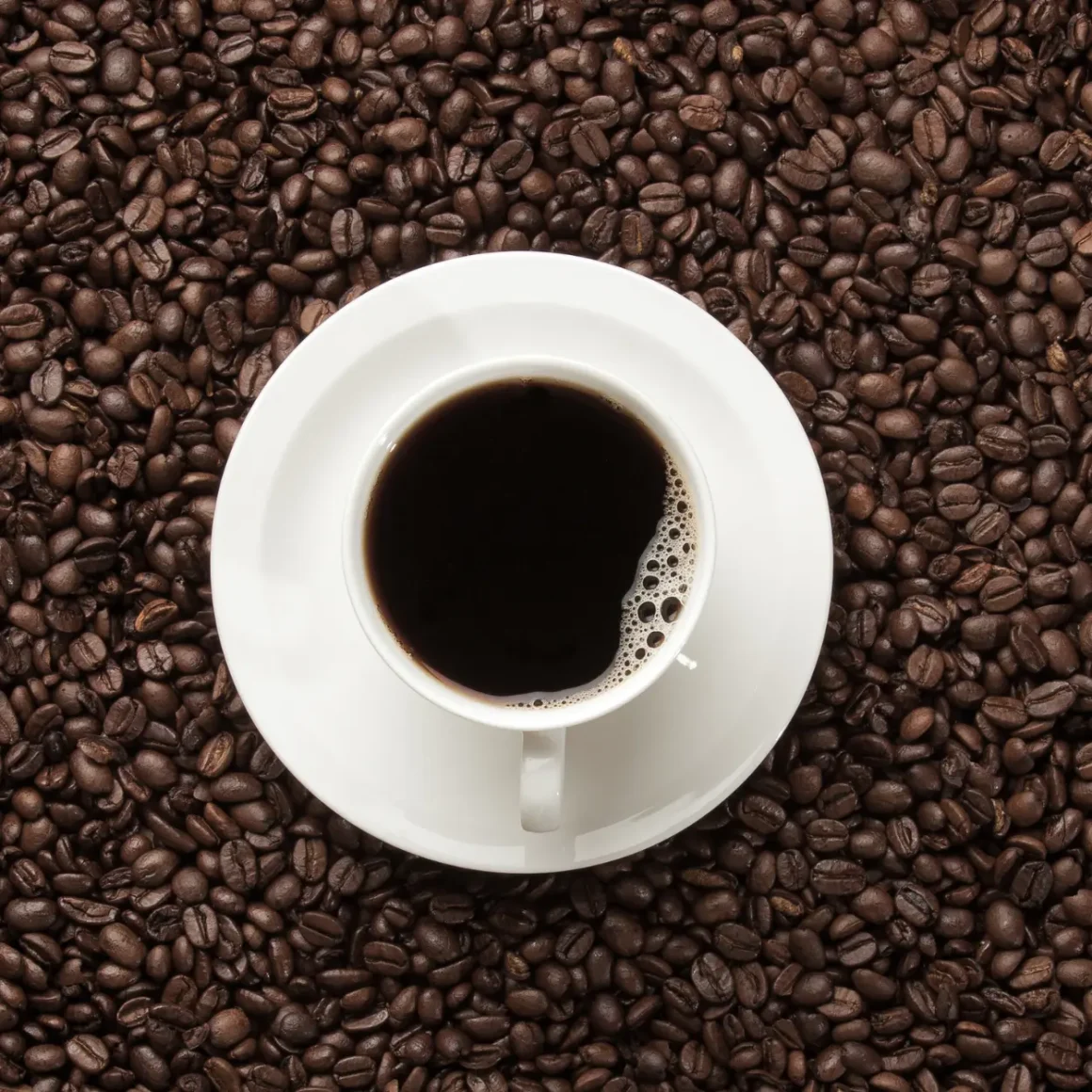 a cup of coffee on a saucer on a pile of dark roast coffee beans