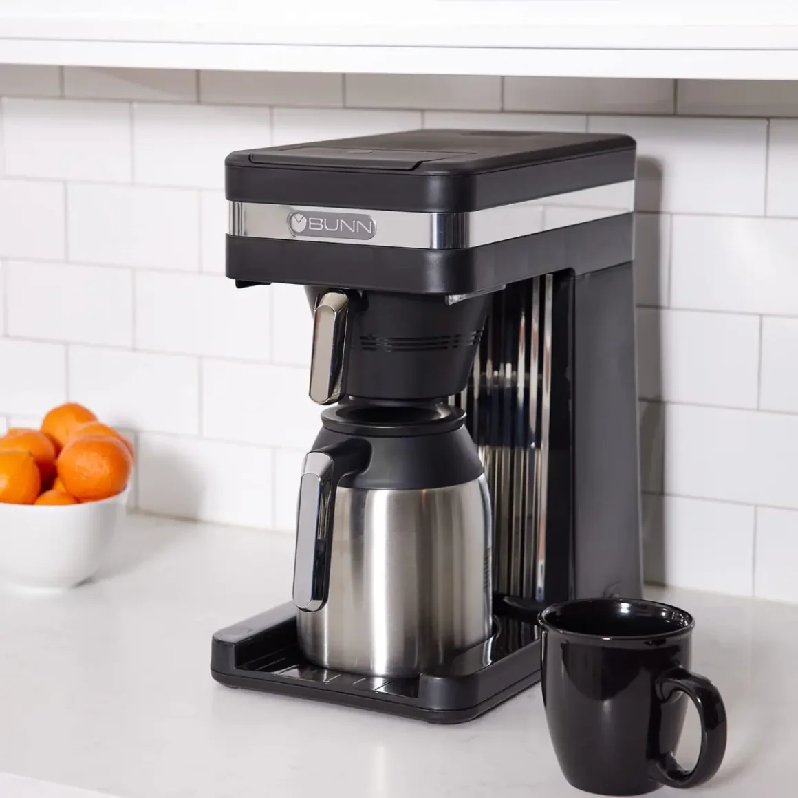 a bunn 55200 CSB3T coffee maker with a black cup and a bowl of oranges on a counter