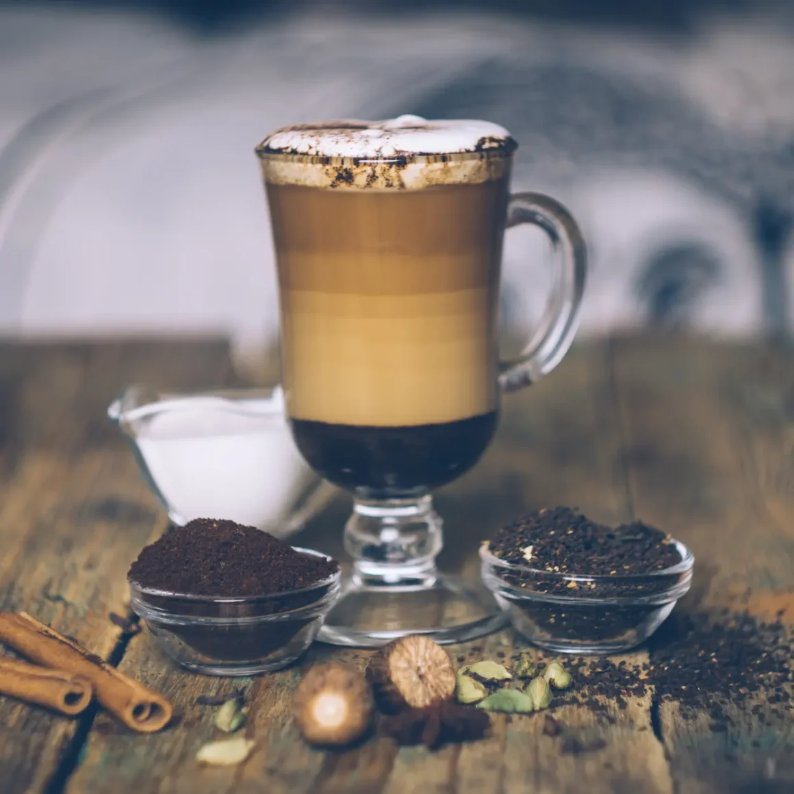 a glass cup of dirty chai latte and a few bowls of ground coffee