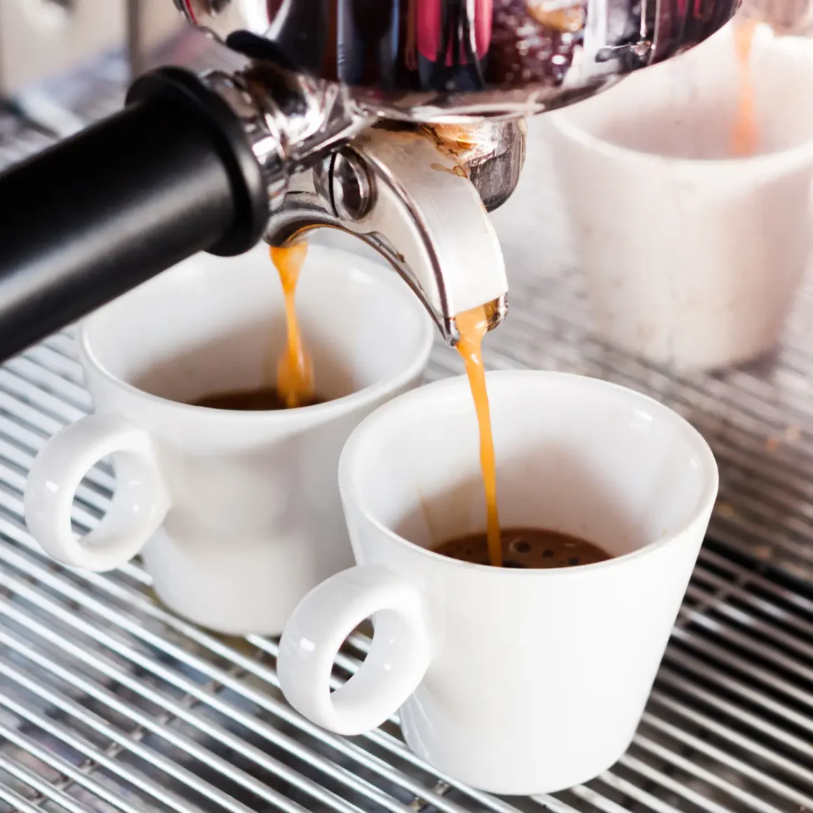 a espresso machine pouring coffee into two white cups