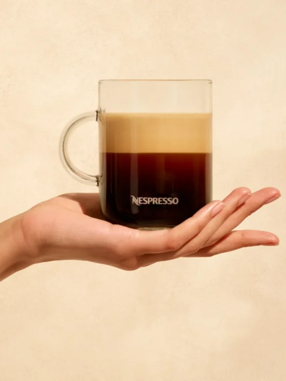 a hand holding a glass cup of gran lungo coffee