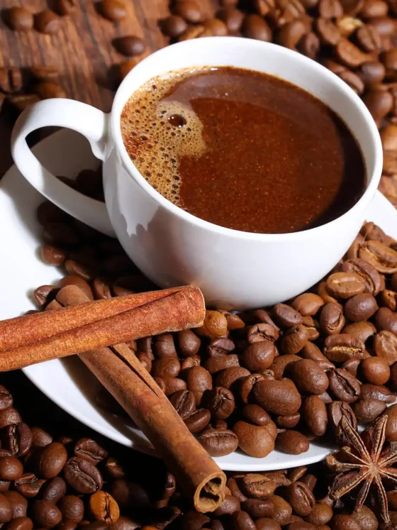 a cup of coffee on a saucer with beans and cinnamon sticks