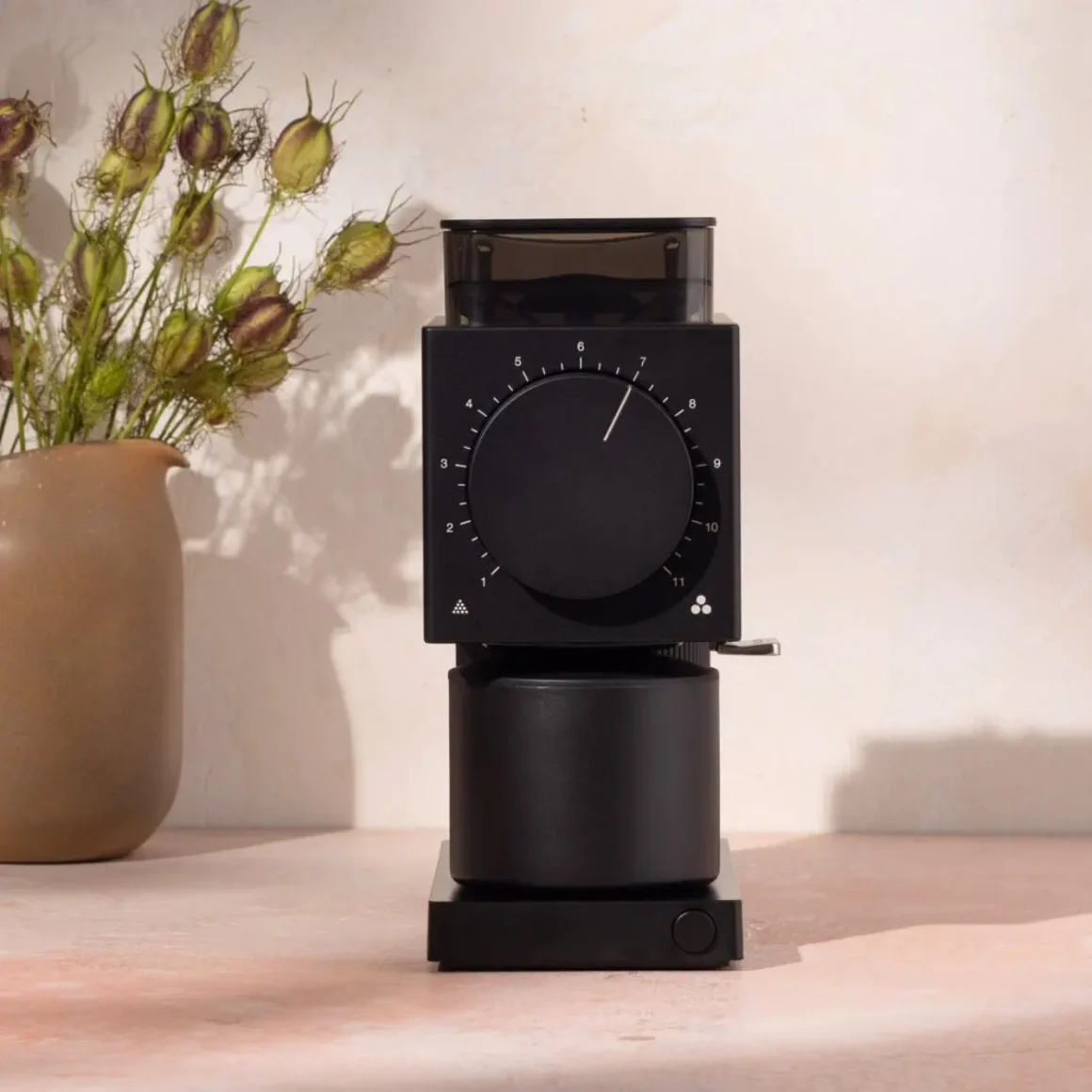 a black fello ode brew coffee grinder with a black dial and a brown vase of flowers