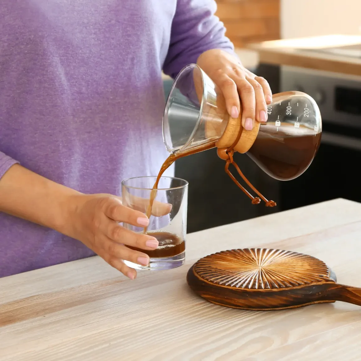 a person pouring coffee from a chemex coffee maker into a glass