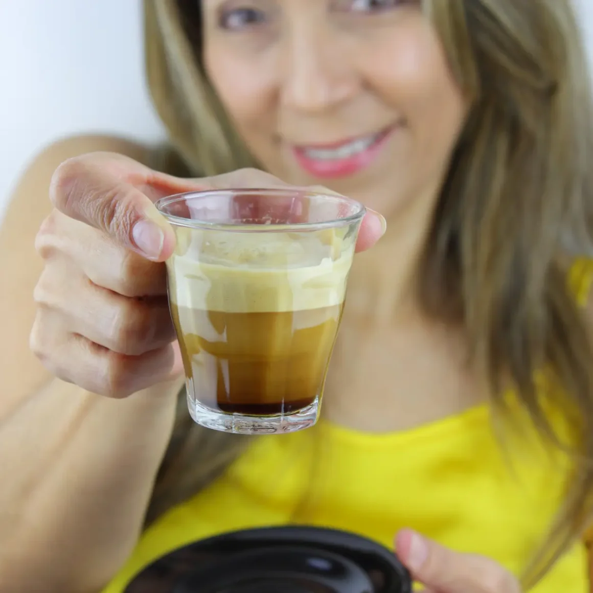 a woman holding a glass of cortado coffee