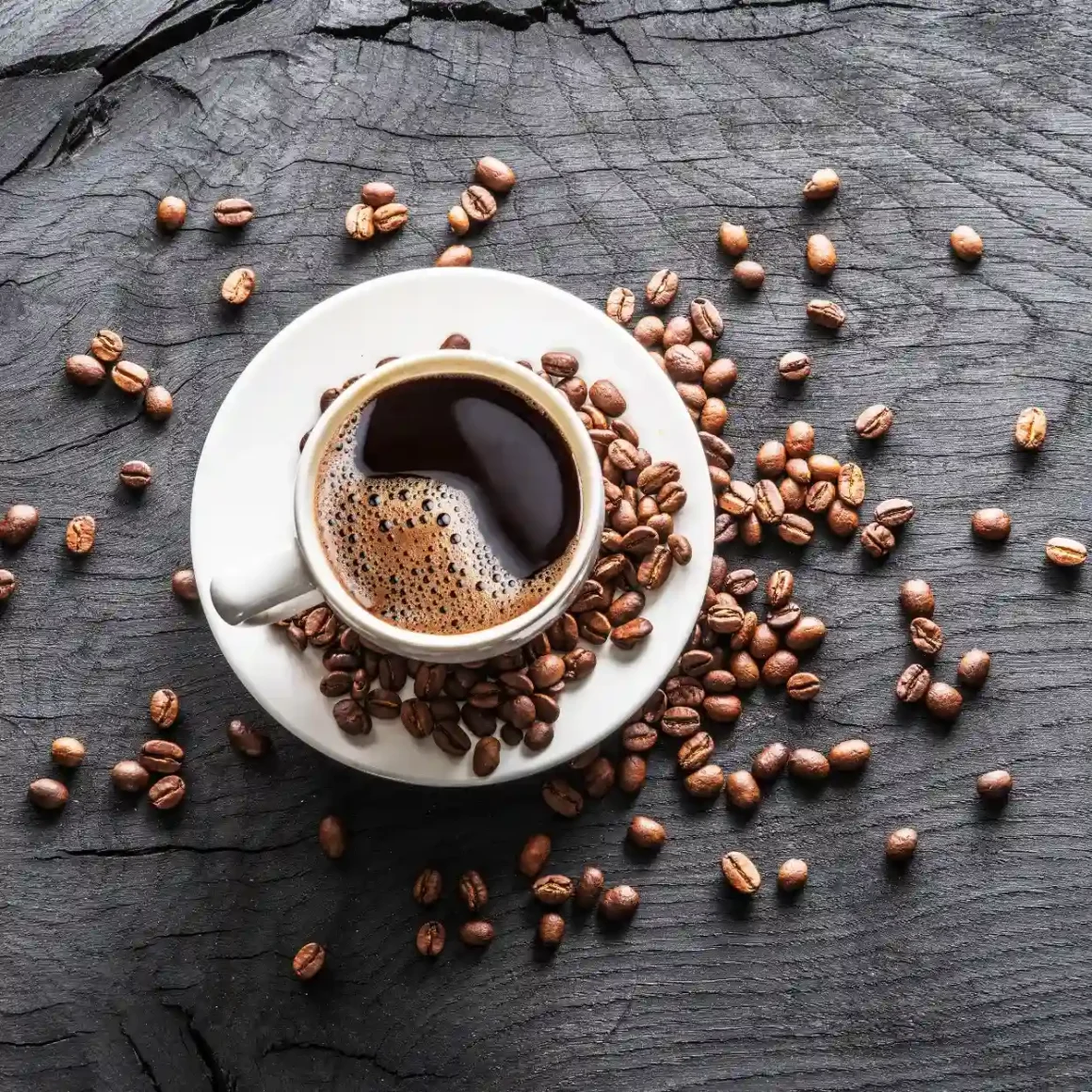 cup of coffee on a saucer with medium roast coffee beans around it