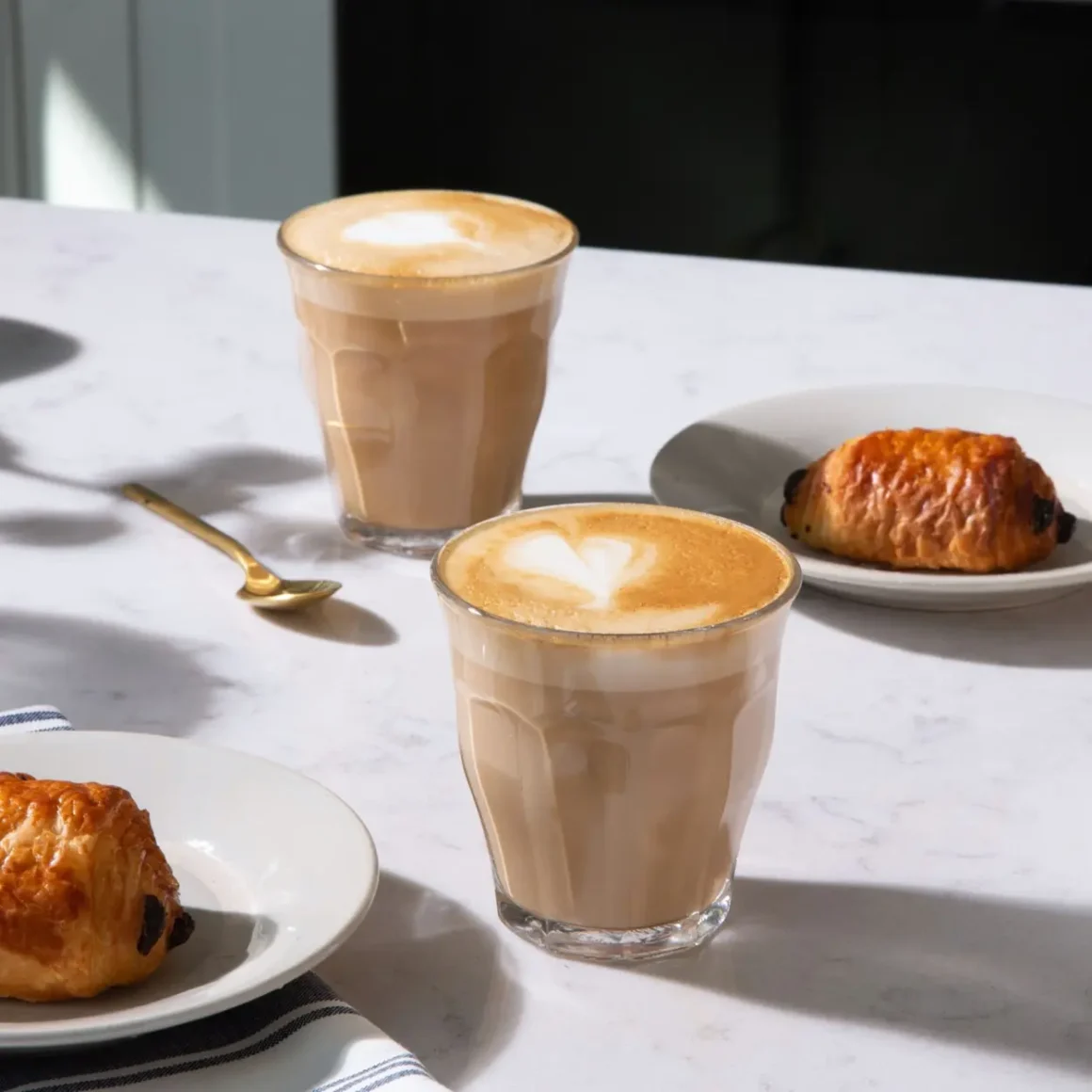 a table with a glass of cortado coffee and gibraltar coffee with croissants