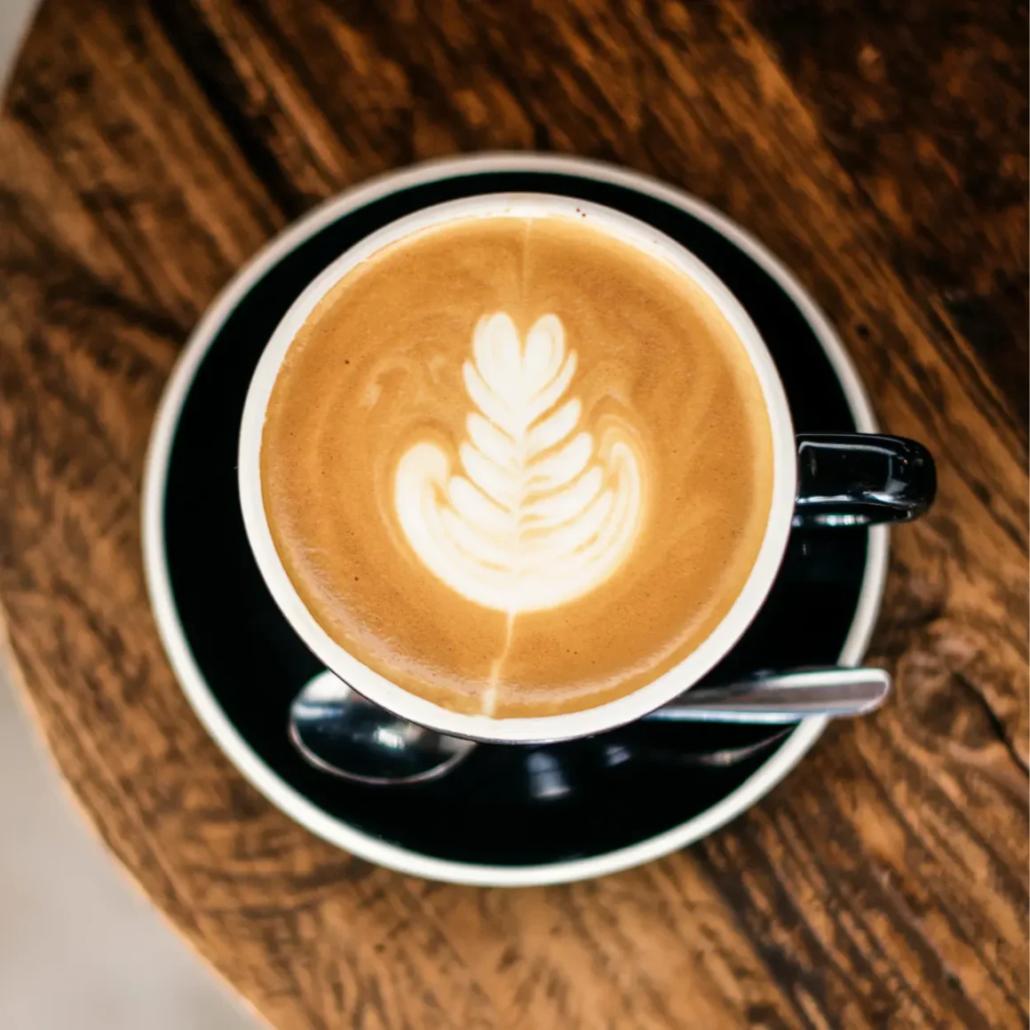 a cup of wet cappuccino coffee with a leaf design in the foam