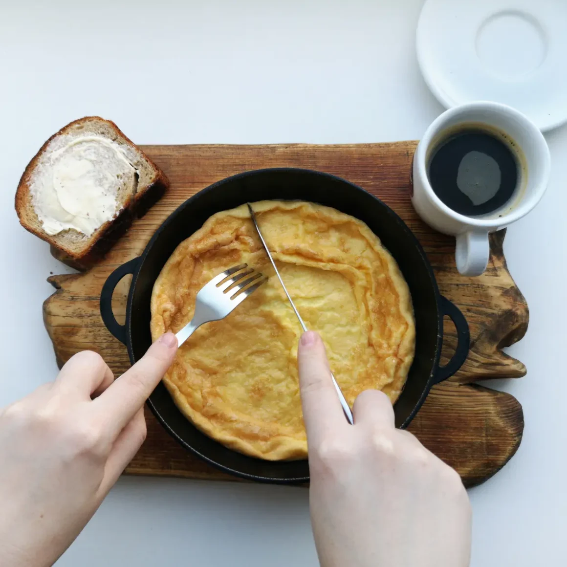a person holding a fork and knife cutting an omelette with a cup of americano coffee
