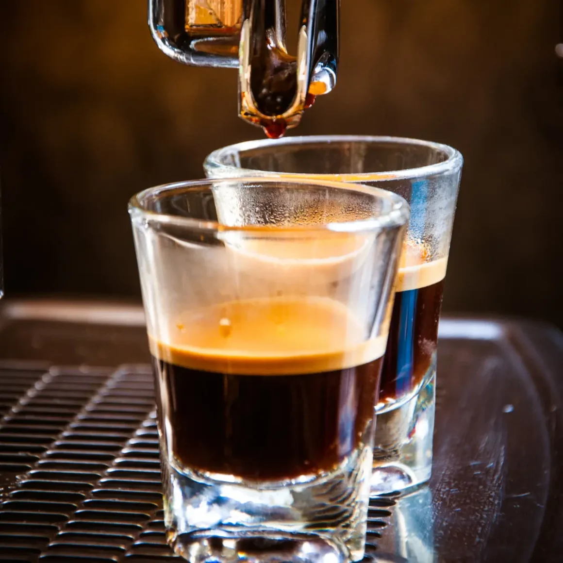 an espresso machine pouring coffee into shot glasses