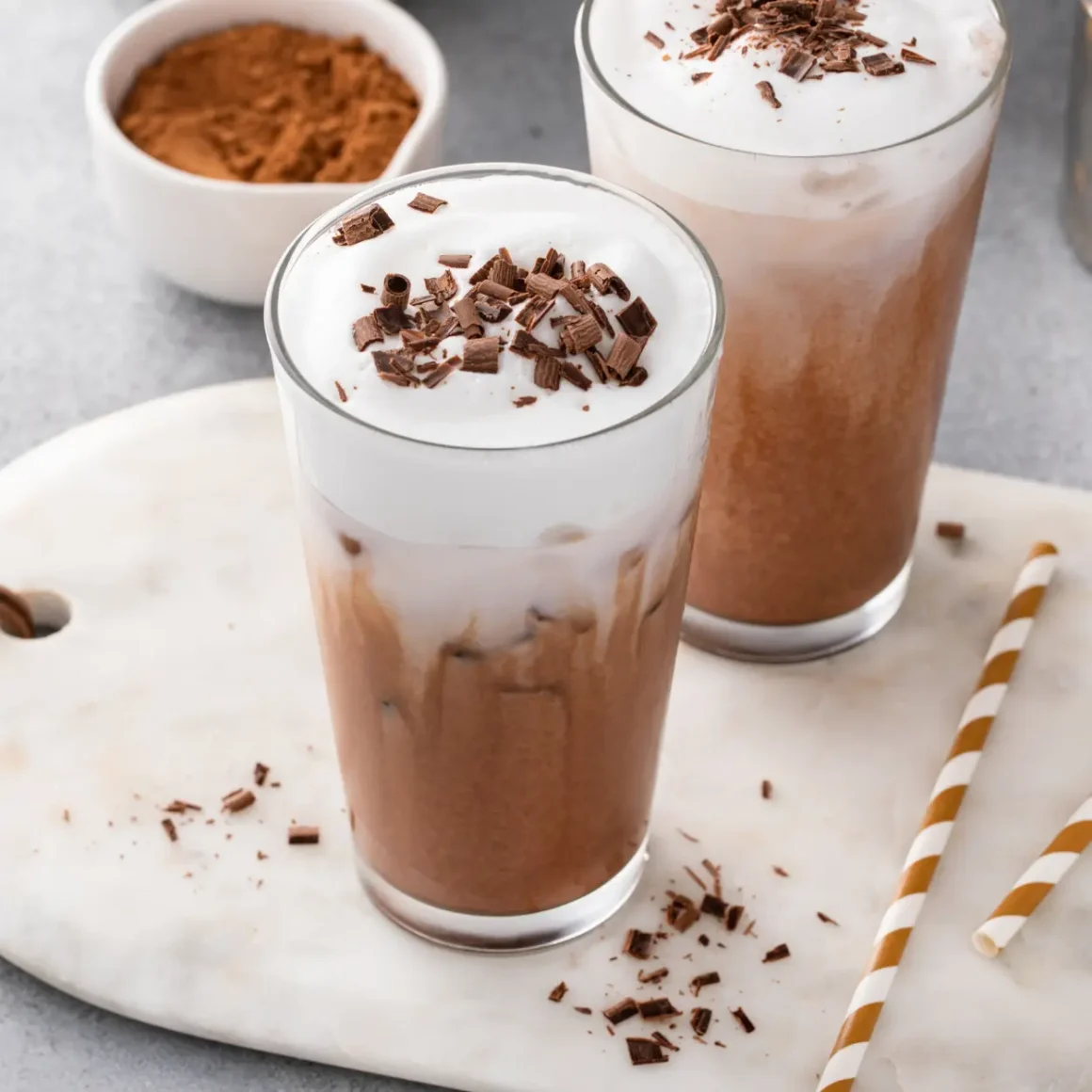 two glasses of chocloate milkshakes with whipped cream and straws