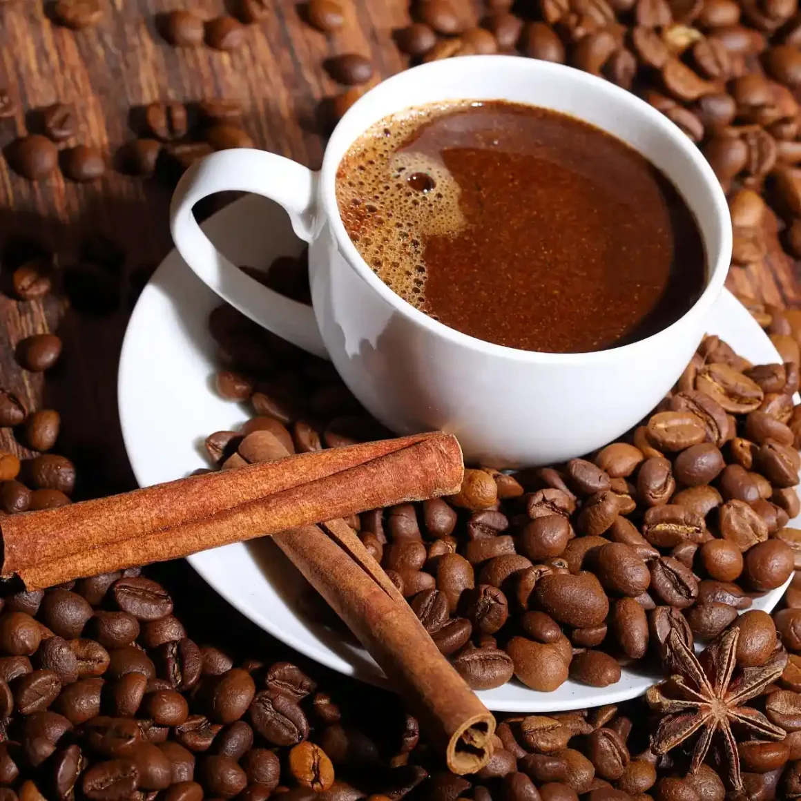 a cup of coffee on a saucer with beans and cinnamon sticks
