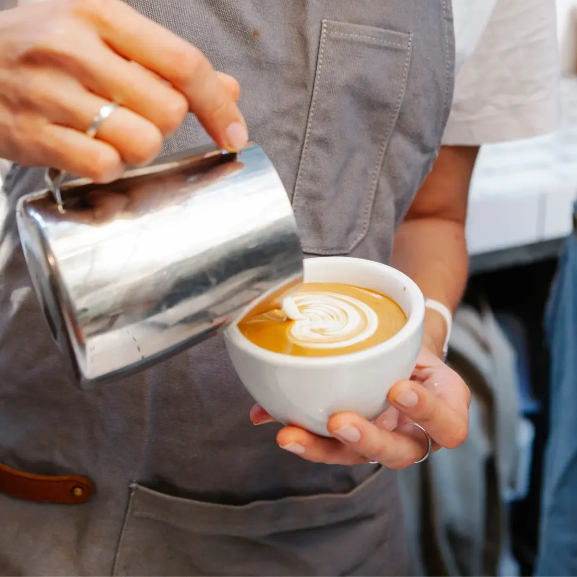 barista preparing cappuccino by pouring milk into a cup of coffee