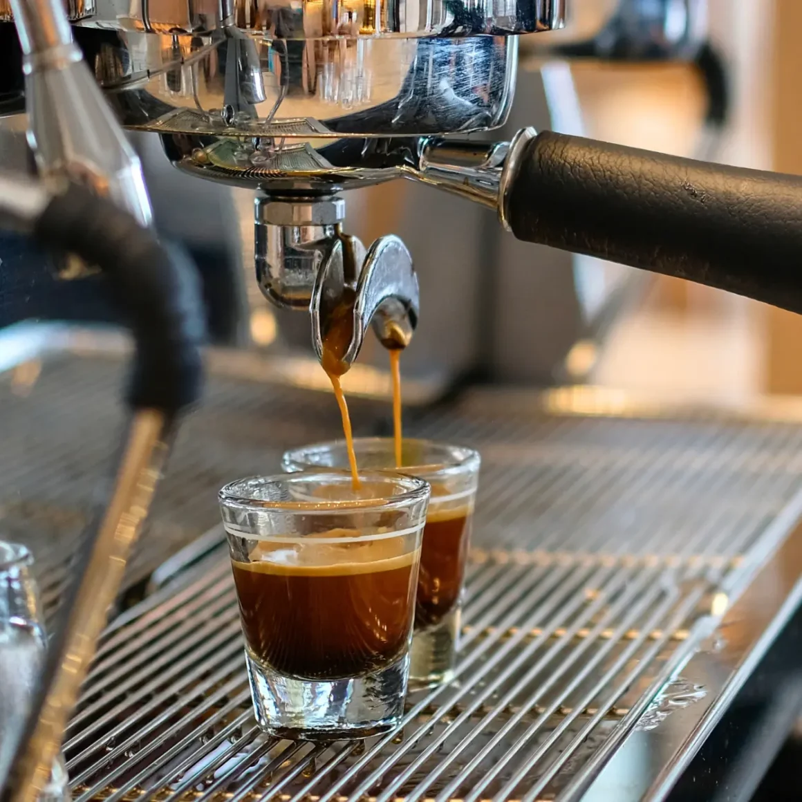 a espresso machine pouring macchiato coffee into shot glasses