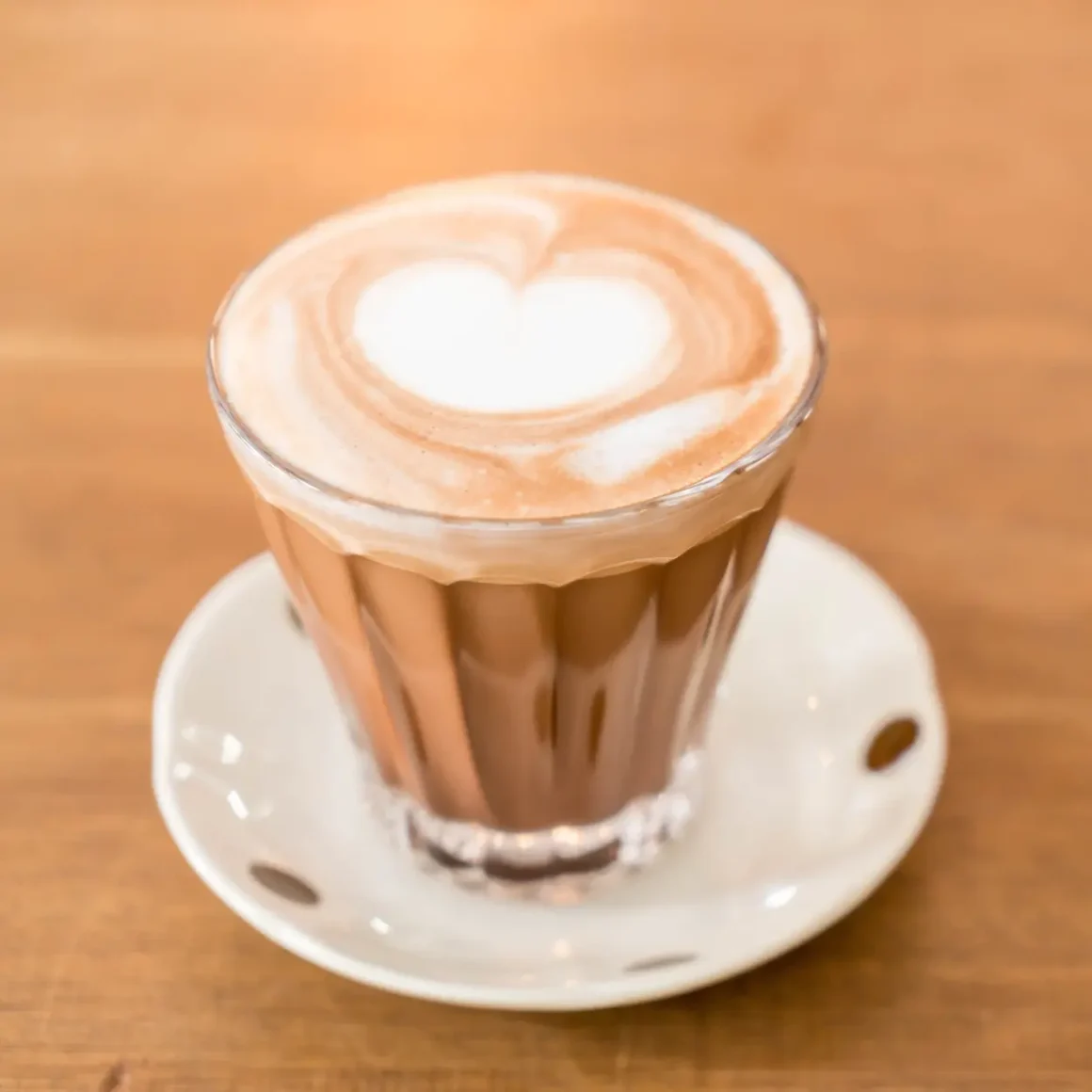 a glass of cortado coffee with a heart design in the foam