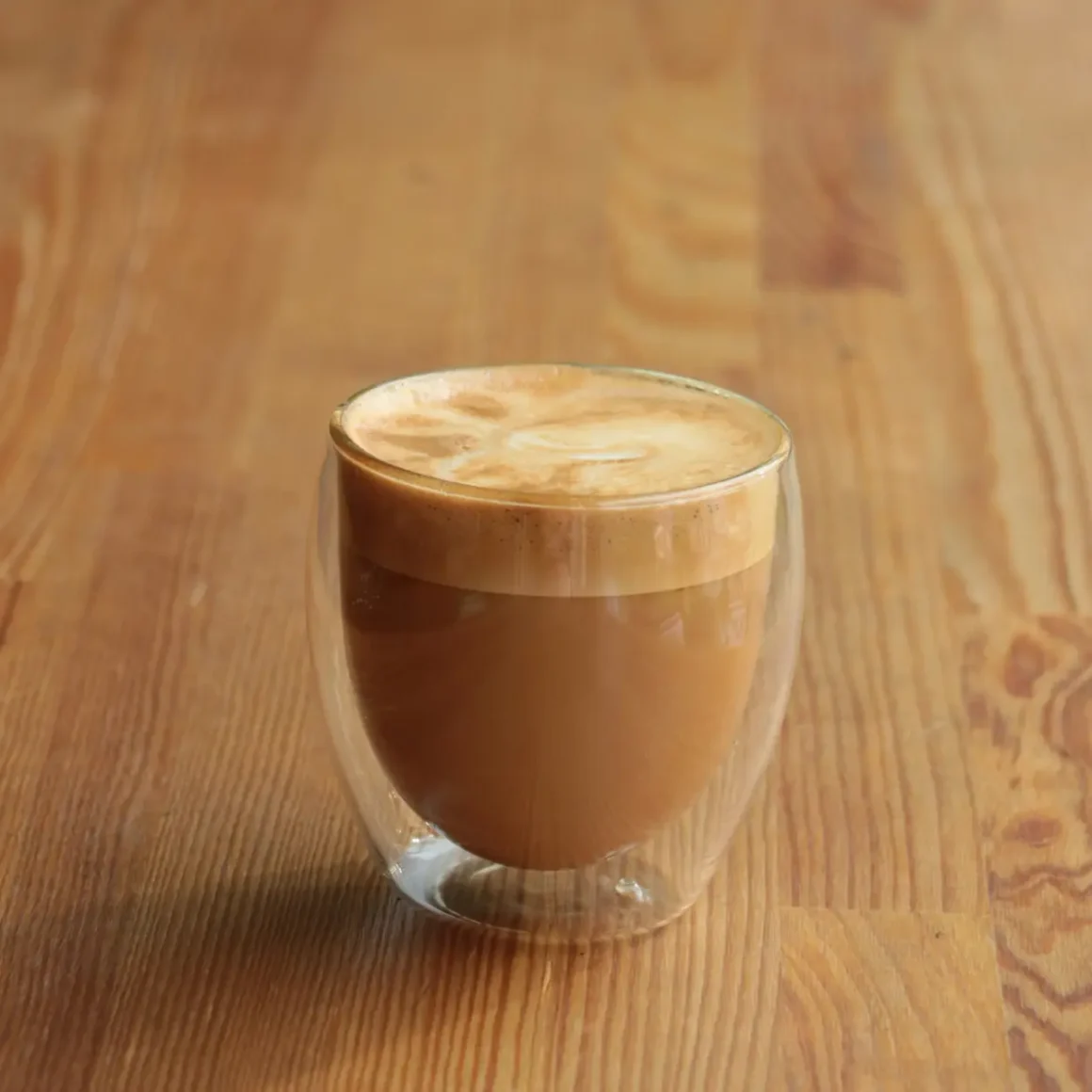 a glass cup with a gibraltar coffee on a wooden surface