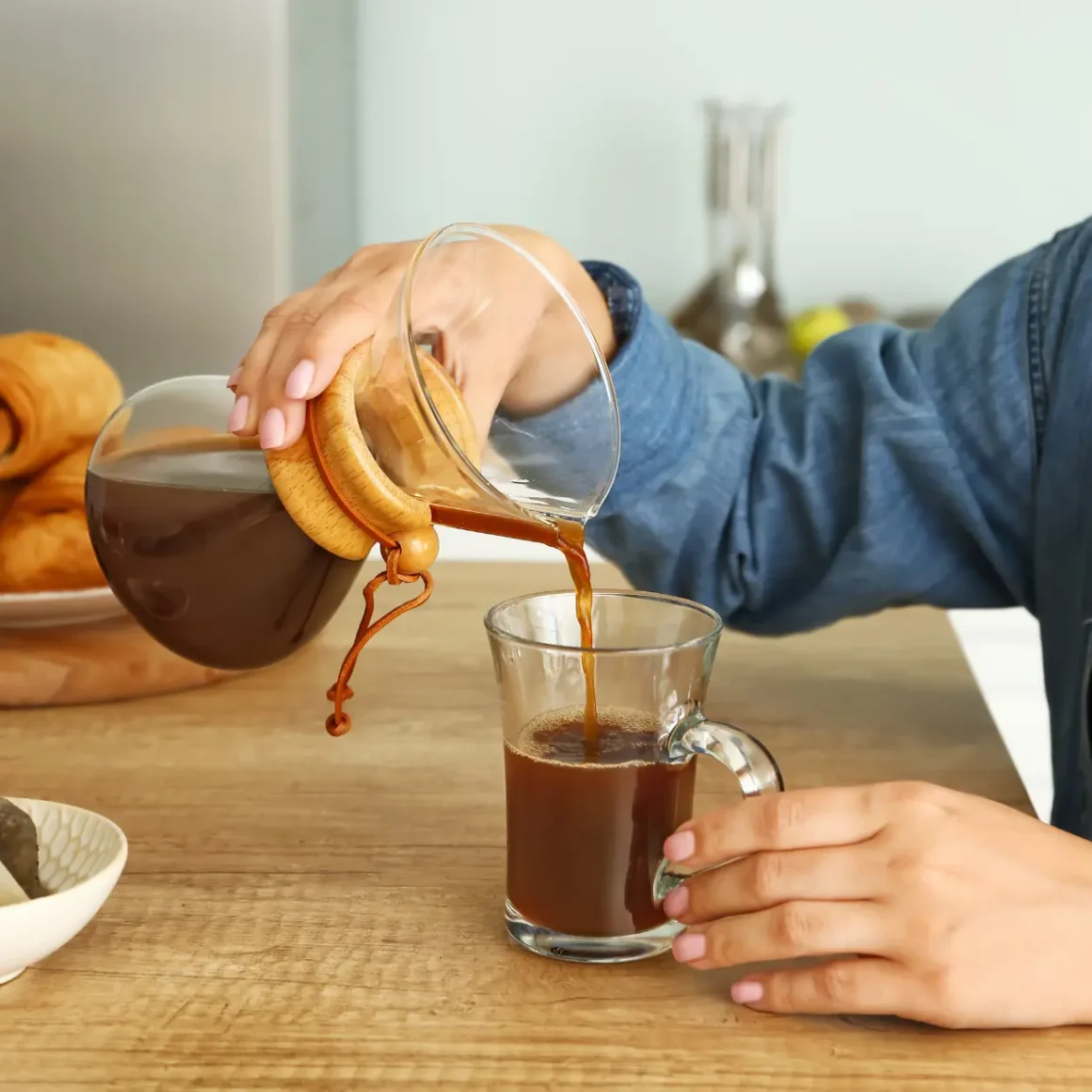 a person pouring coffee from a chemex coffee maker into a glass