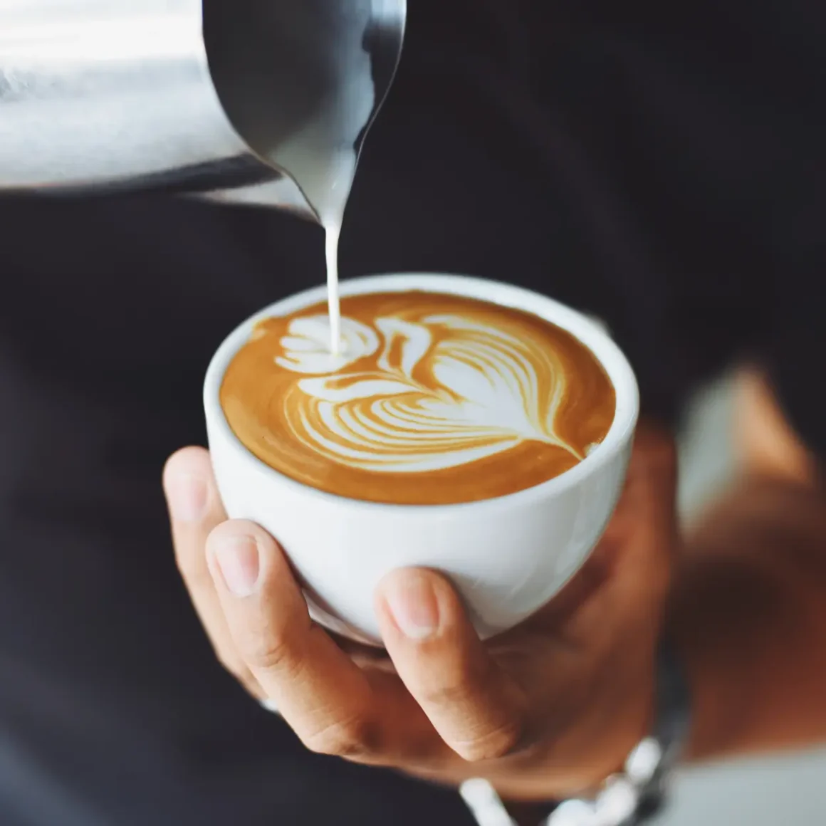 barista pouring forthed milk into a cup of coffee