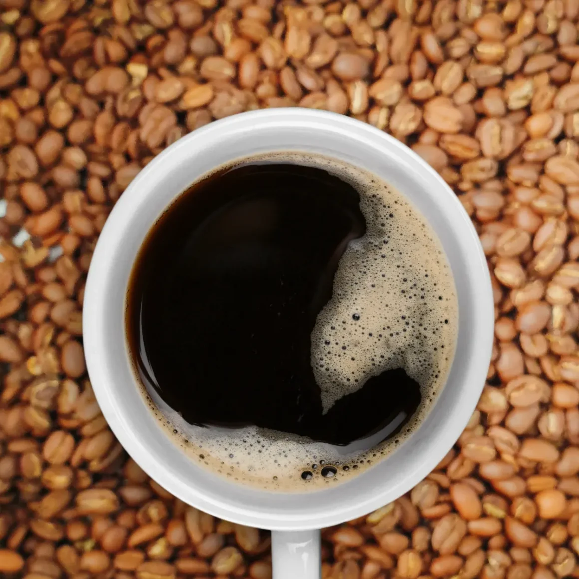 a cup of coffee on a saucer on a pile of light roast coffee beans
