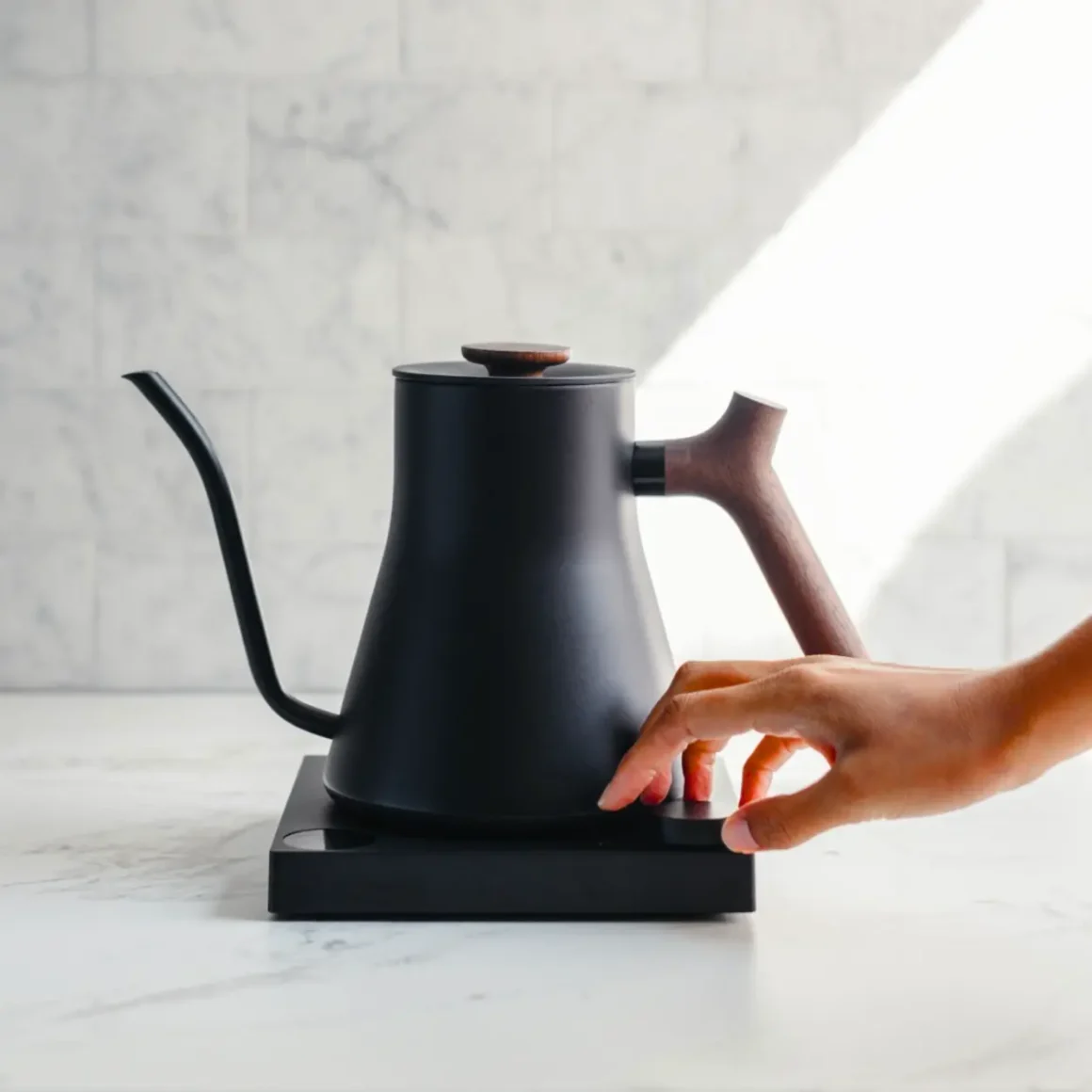 a hand touching a black fellow stagg ekg electric kettle