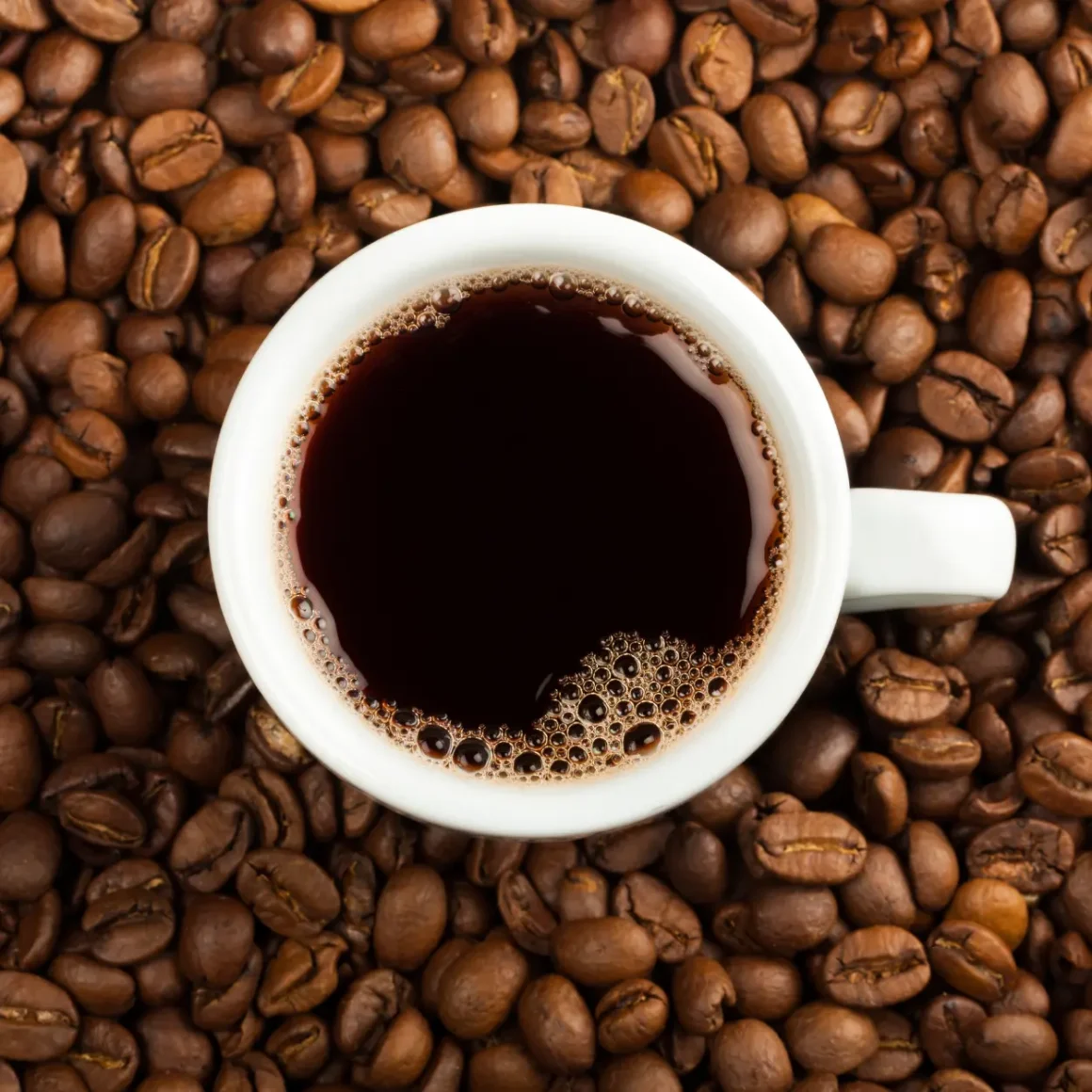 a cup coffee with a spoon over a pile of medium roast coffee beans