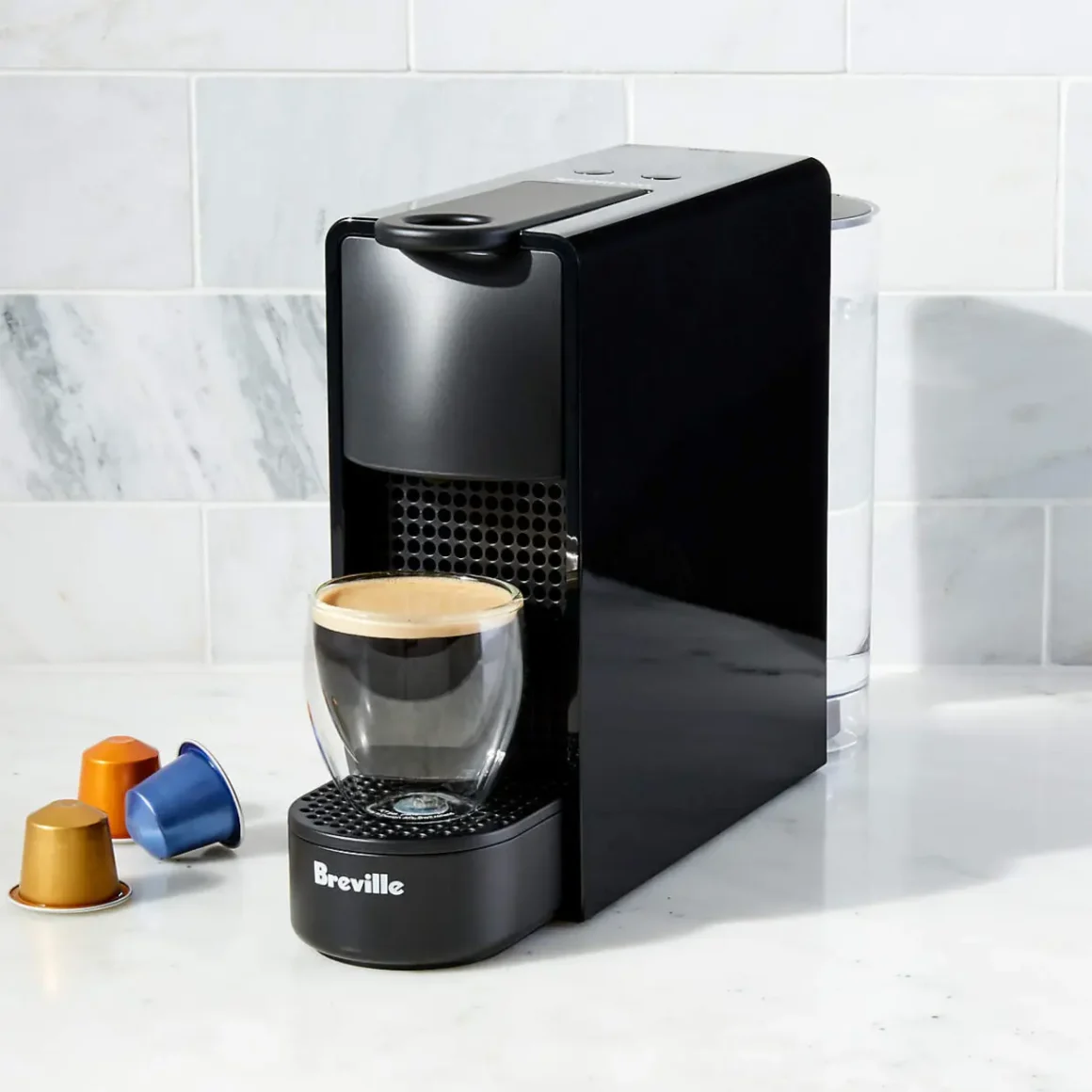 a black nespresso essenza mini espresso machine with a glass cup and coffee capsules