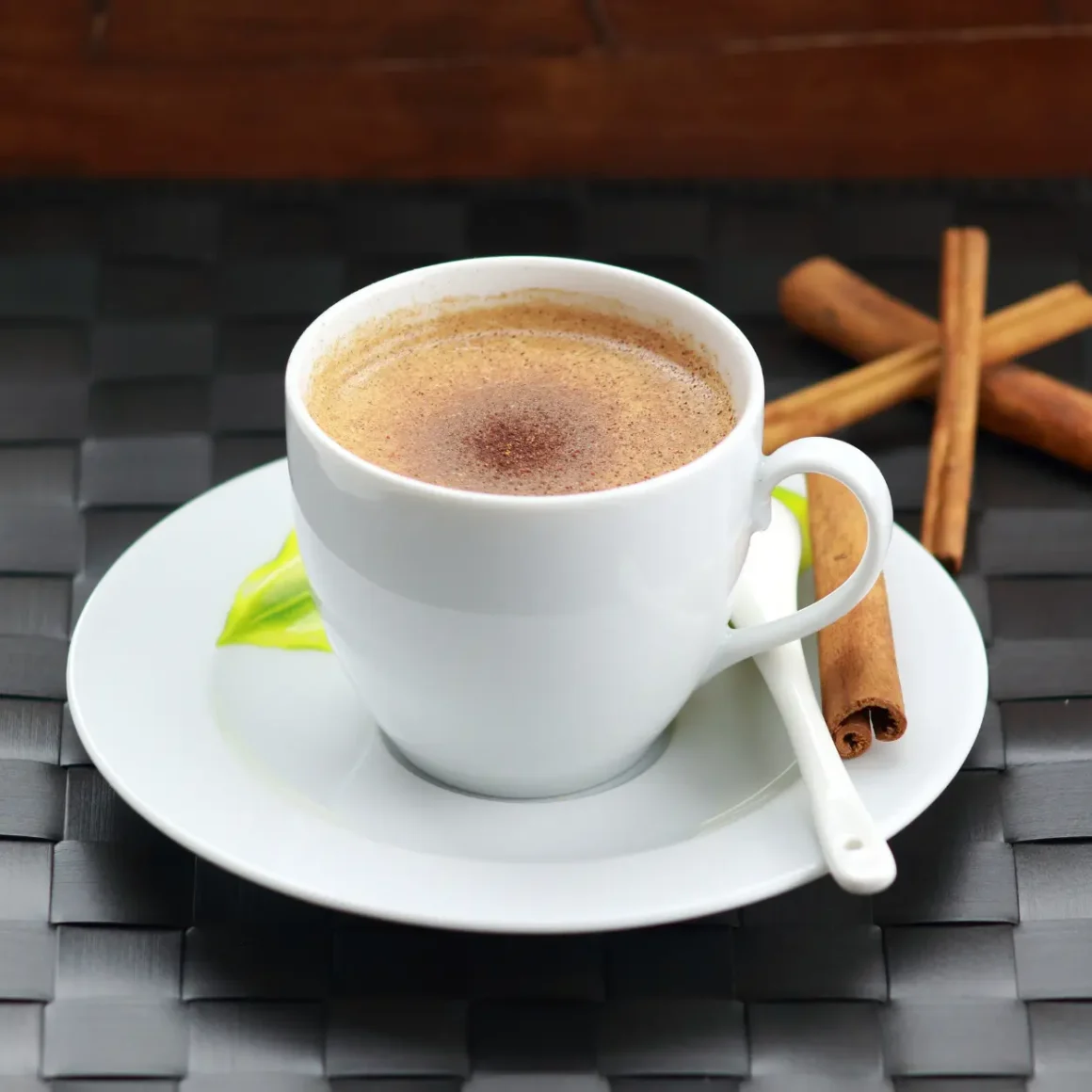 a cup of coffee with cinnamon sticks and a leaf