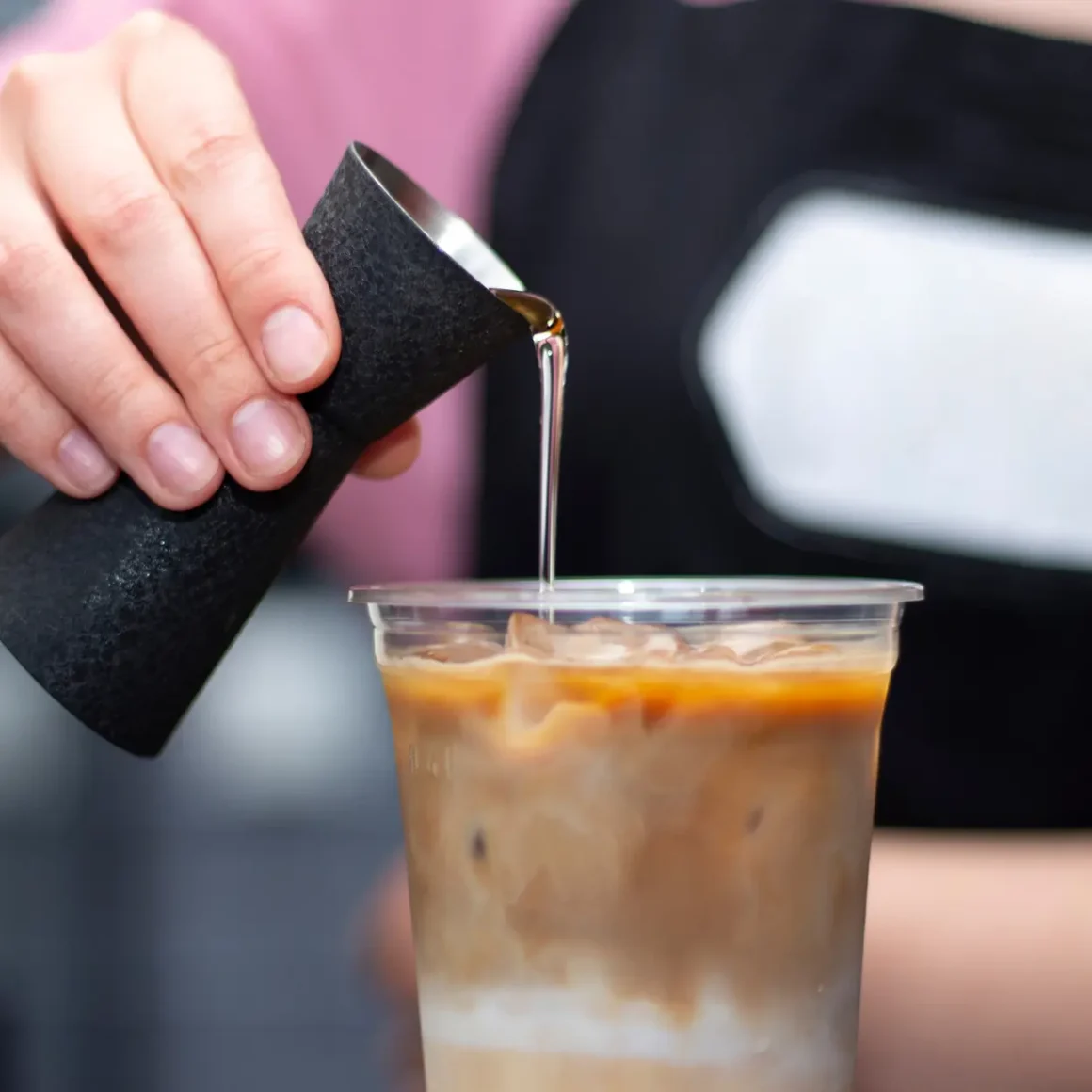 a person pouring coffee syrups into a cup of coffee