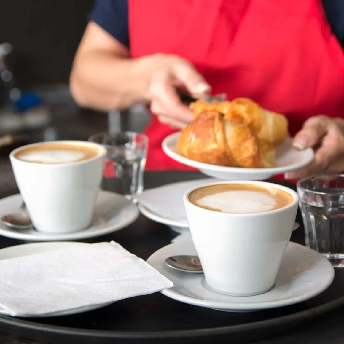 a person holding a plate of croissant with the cups of latte