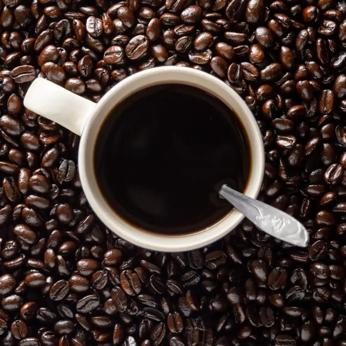 a cup of coffee with a spoon on a full city roast coffee beans