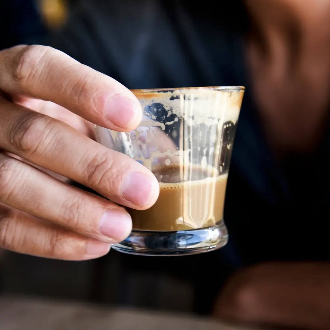 a hand holding a glass of cortado coffee