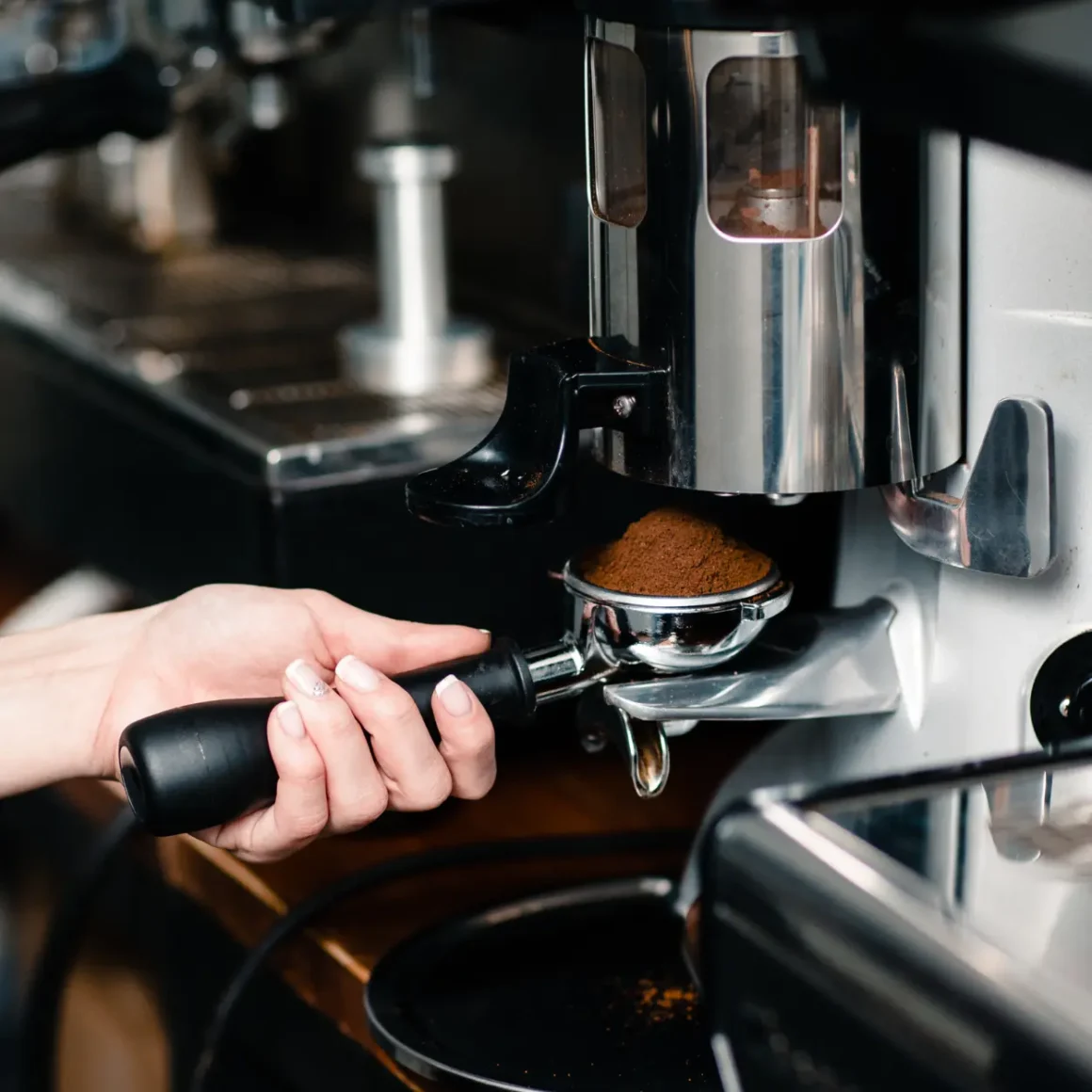 barista holding a portafilter in front of an espresso machine