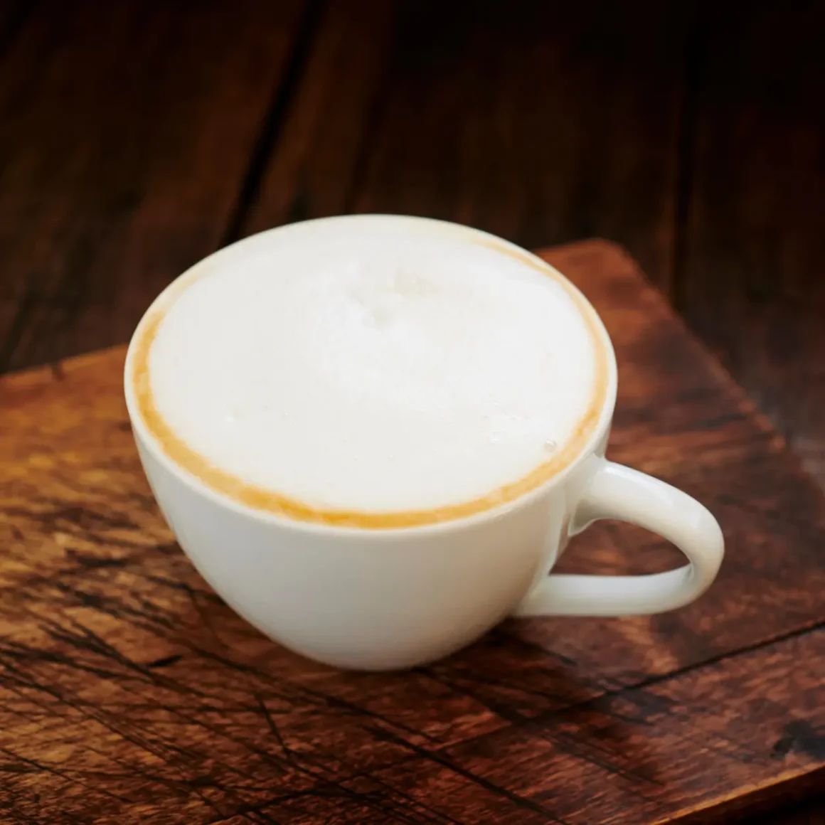 a white cup of dry cappuccino coffee on a wooden surface